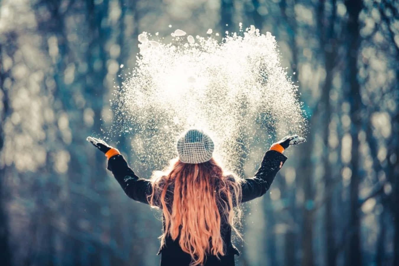 冬季 桌布 壁紙 — 一位長粉紅色頭髮的人在冬季森林中向太陽扔雪，雪花在金色逆光中閃耀。