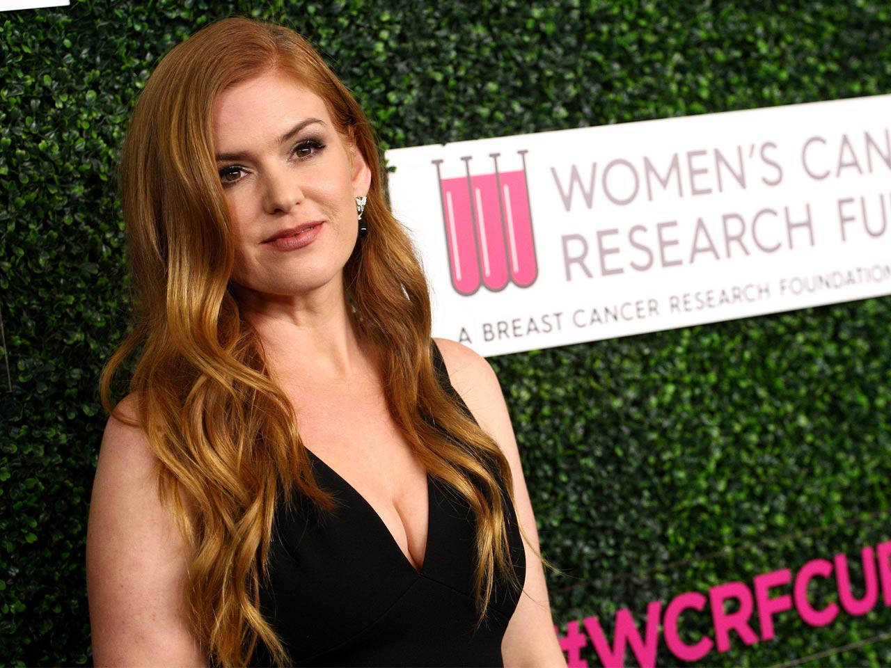Celebrity 桌布 壁紙 — 一位長紅髮、身穿黑色連衣裙的女性站在綠色樹籬牆前，旁邊有女性癌症研究基金會的標誌。