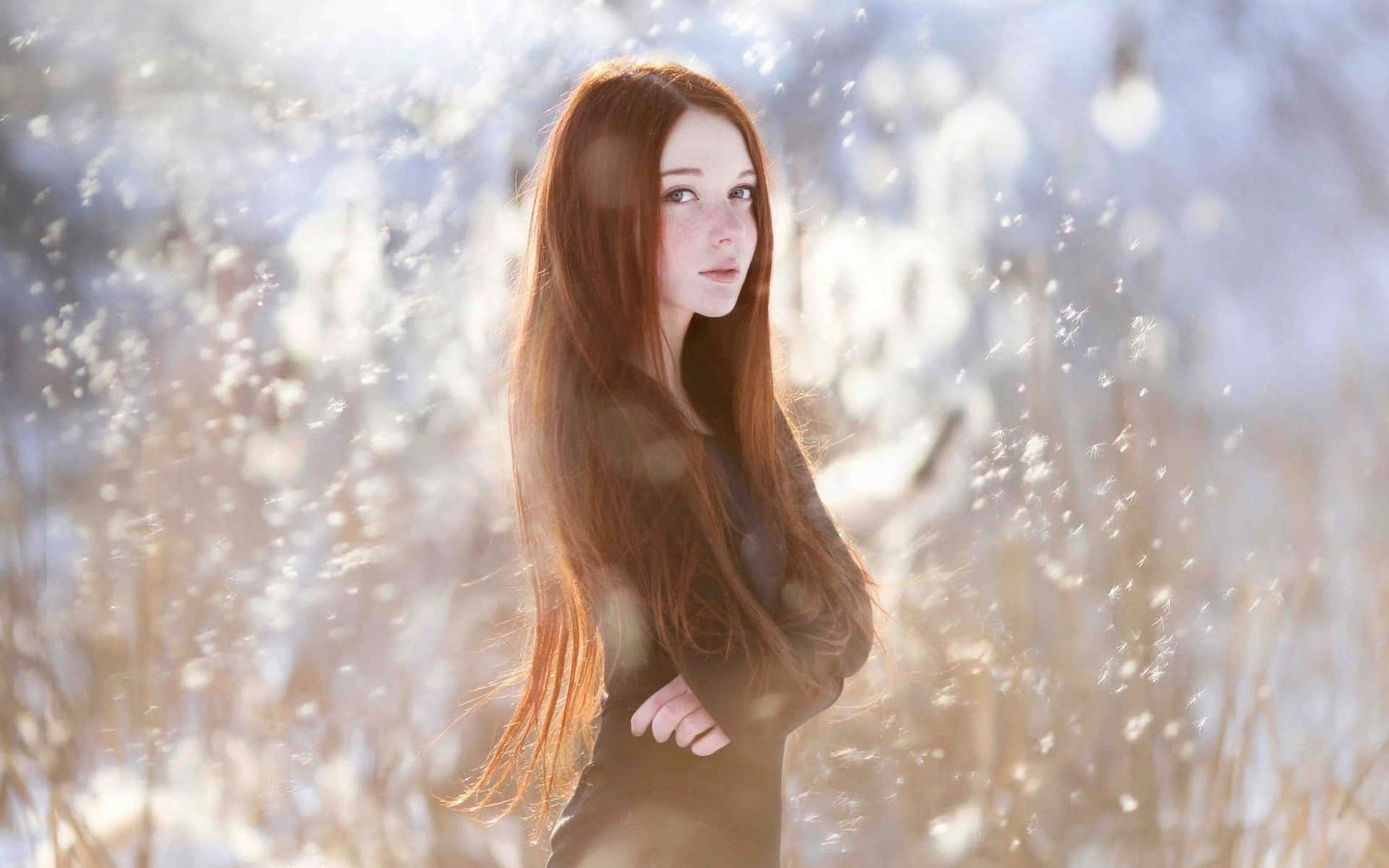 Photoshoot 桌布 壁紙 — 一位長紅髮的年輕女子站在陽光明媚的高草田野中，閃爍的粒子漂浮在她周圍。