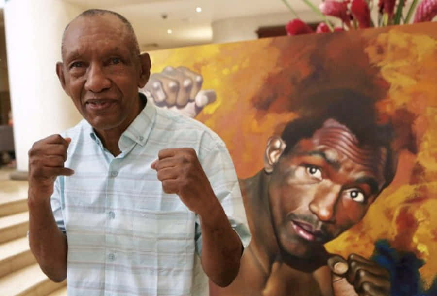 Boxing 桌布 壁紙 — 一位長者在色彩鮮豔、帶有火熱橙黃色調的拳擊手壁畫前模仿拳擊姿勢。