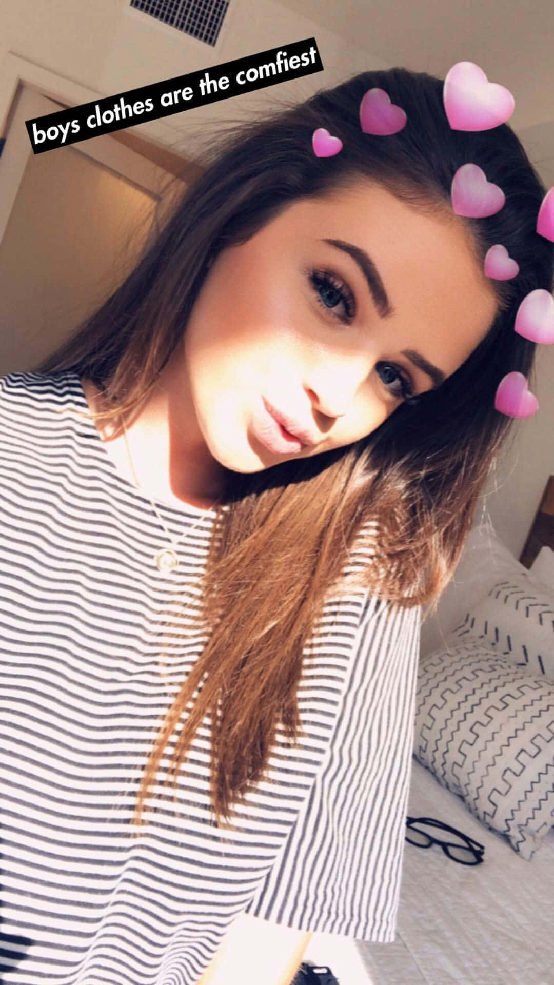 Snapchat 桌布 壁紙 — 一位長著棕色長髮、帶有粉紅色心形濾鏡的年輕女性，在臥室裡穿著條紋襯衫，溫柔地微笑。