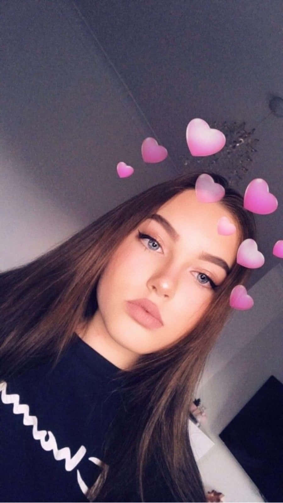 Snapchat 桌布 壁紙 — 一位長著棕色長髮和藍色眼睛的年輕女性看著鏡頭，粉紅色的心形濾鏡漂浮在她的頭周圍。