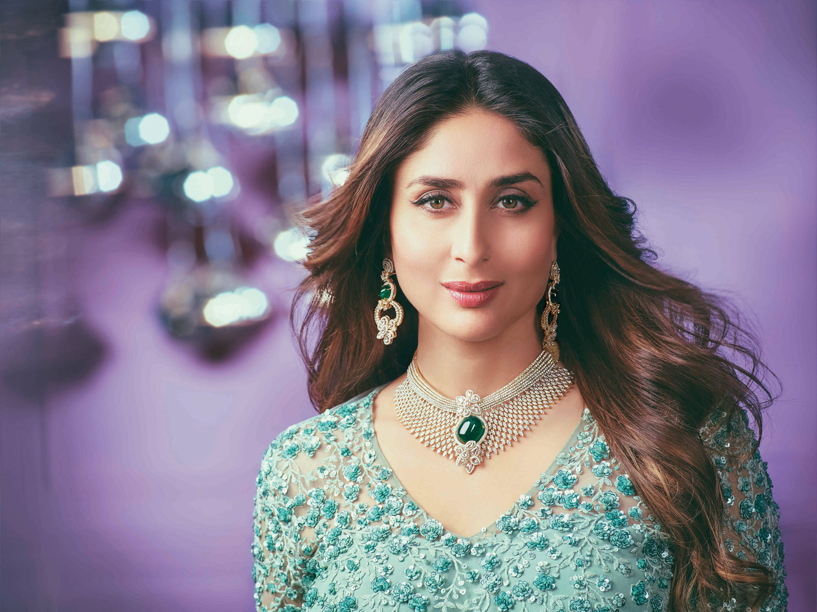 Kareena 桌布 壁紙 — 一位長著棕色長髮的女性，穿著華麗的綠色和銀色珠寶服飾，背景為紫色，帶有散景燈光。
