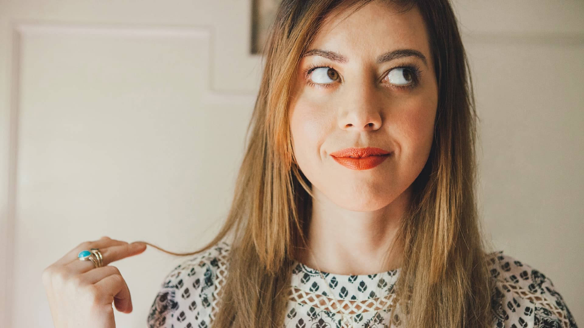 Aubrey 桌布 壁紙 — 一位長著棕色長髮的女性，頑皮地將一縷頭髮夾在手指間，同時向上看，帶著會意的微笑。