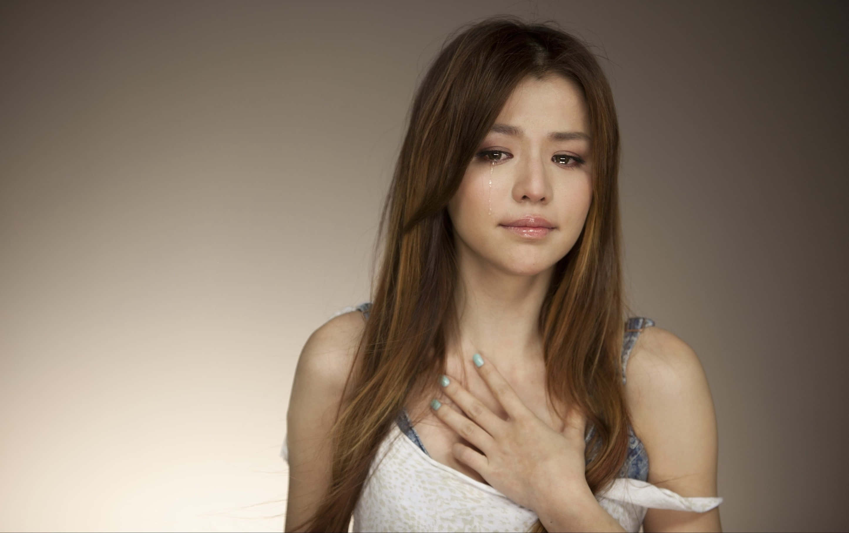 cry 桌布 壁紙 — 一位長著棕色長髮的年輕女性，在柔和的漸變背景前，手按胸口輕輕哭泣。