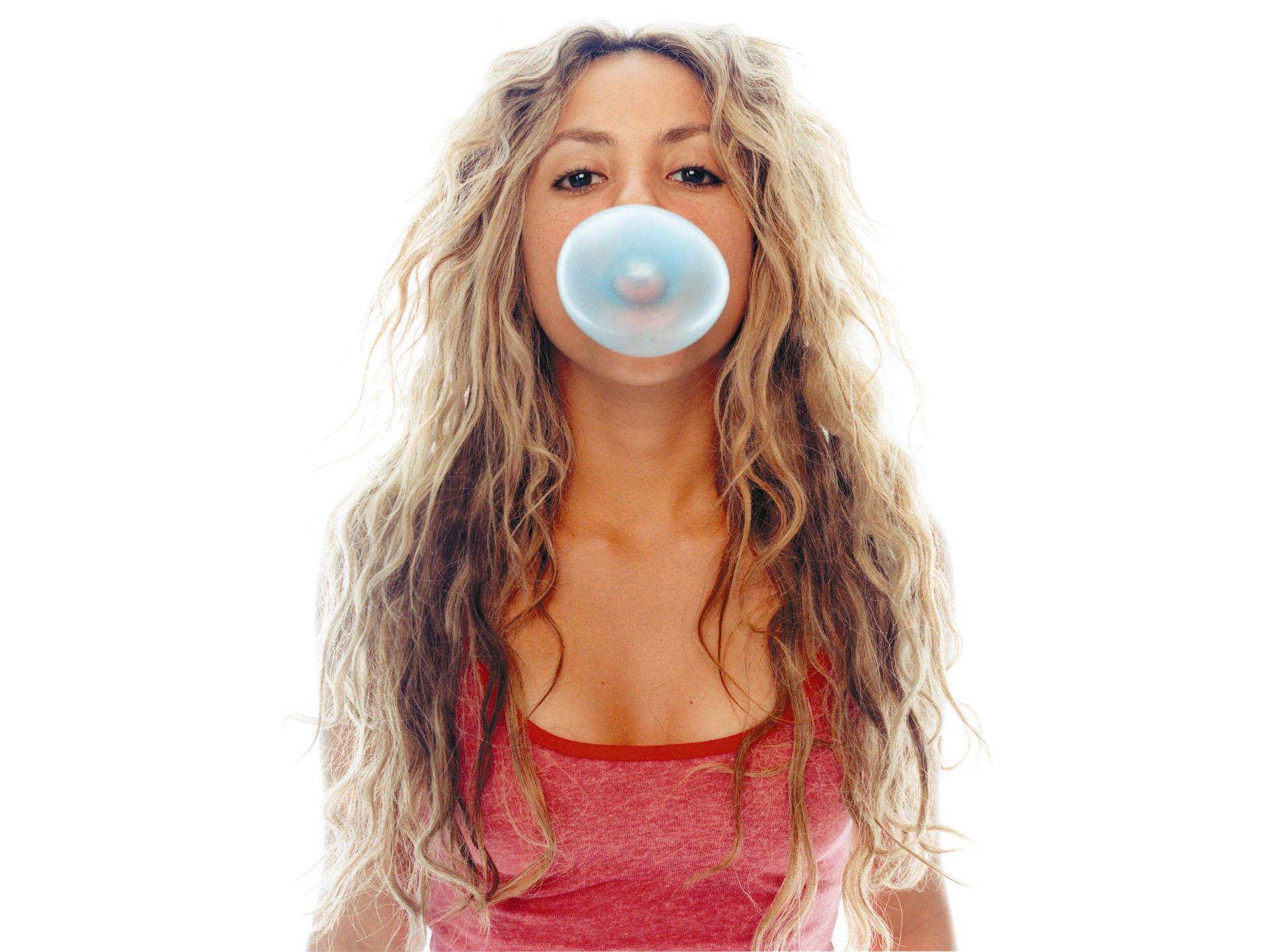 Shakira 桌布 壁紙 — 一位長著波浪長金髮的女性，在純白背景下吹出一個半透明的藍色泡泡糖泡泡。