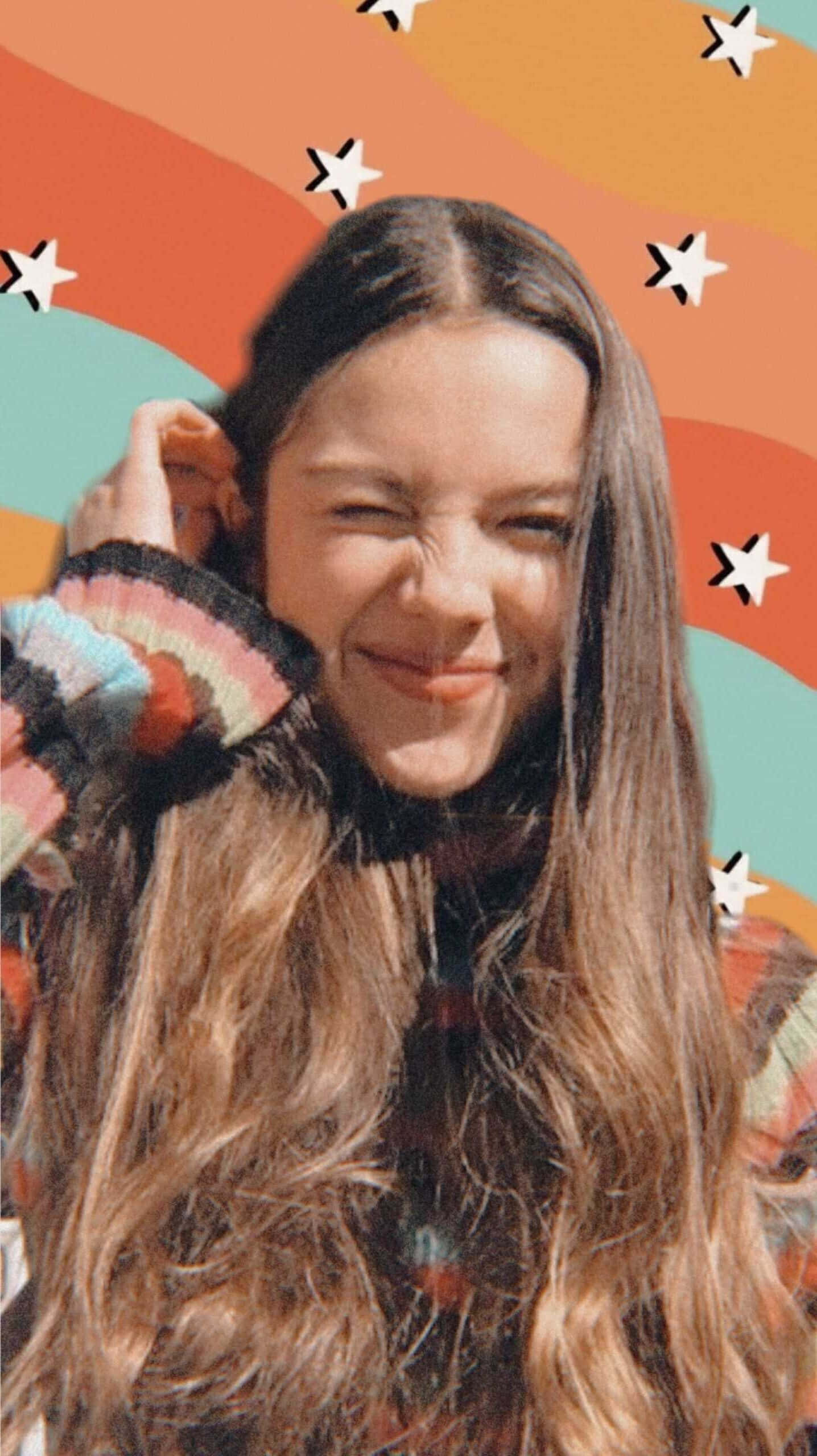 Olivia Rodrigo Aesthetic 桌布 壁紙 — 一位長著波浪長髮的年輕女性，在充滿星星和彩虹條紋的鮮豔抽象背景前俏皮地眨眼。