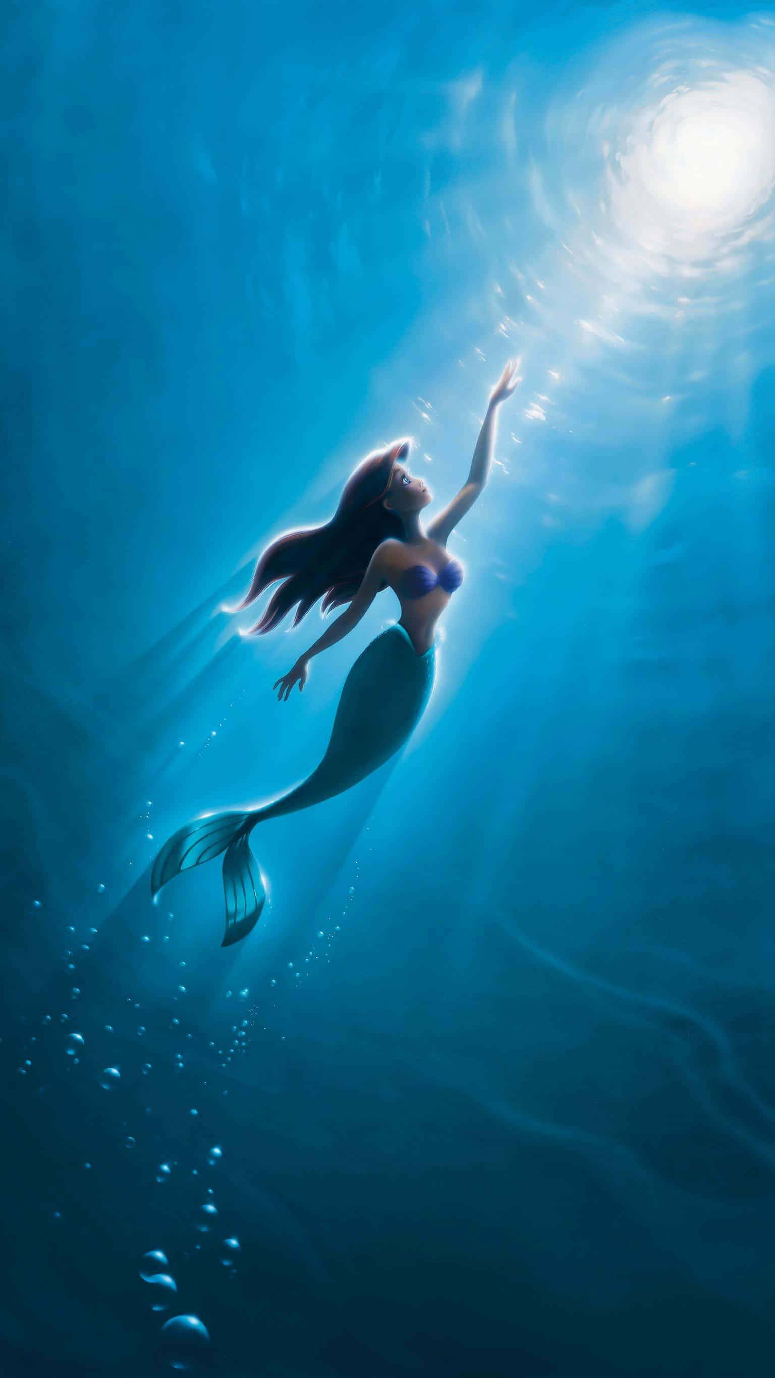 little mermaid 桌布 壁紙 — 一位長著深色長髮的美人魚在深藍色的海水中向上游向明亮的陽光水面。