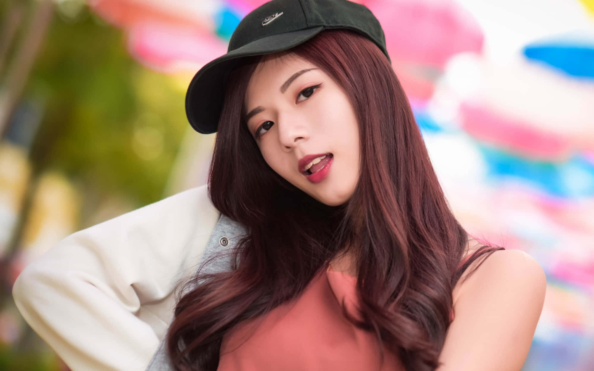 美女 桌布 壁紙 — 一位長著赤褐色長髮、戴著黑色帽子的年輕女性，在色彩繽紛的模糊背景前溫柔地凝視鏡頭。