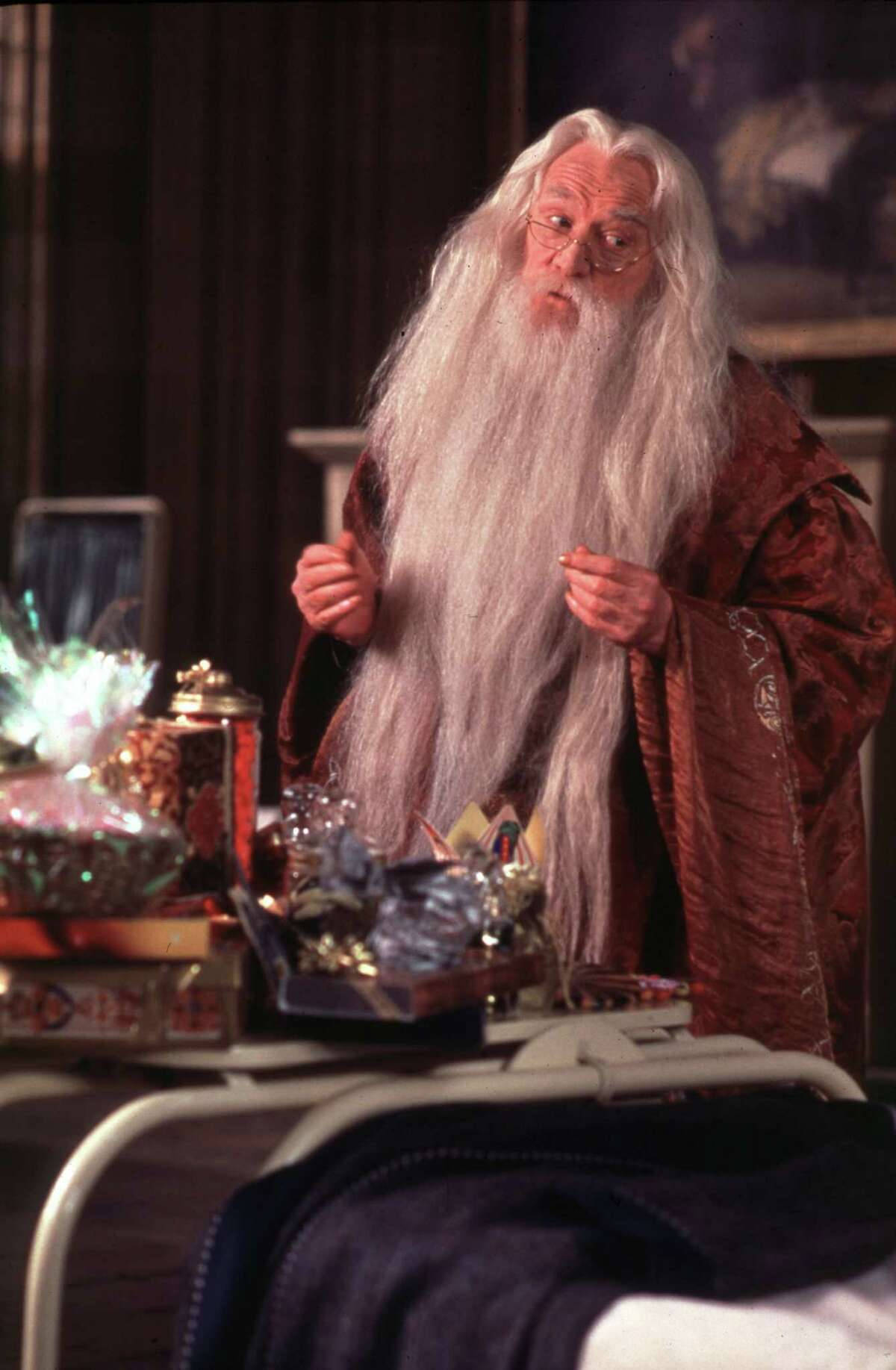 dumbledore 桌布 壁紙 — 一位長著長長白鬍鬚、戴著眼鏡的年長巫師站在一個雜亂的辦公室裡，周圍環繞著魔法文物和發光物體。