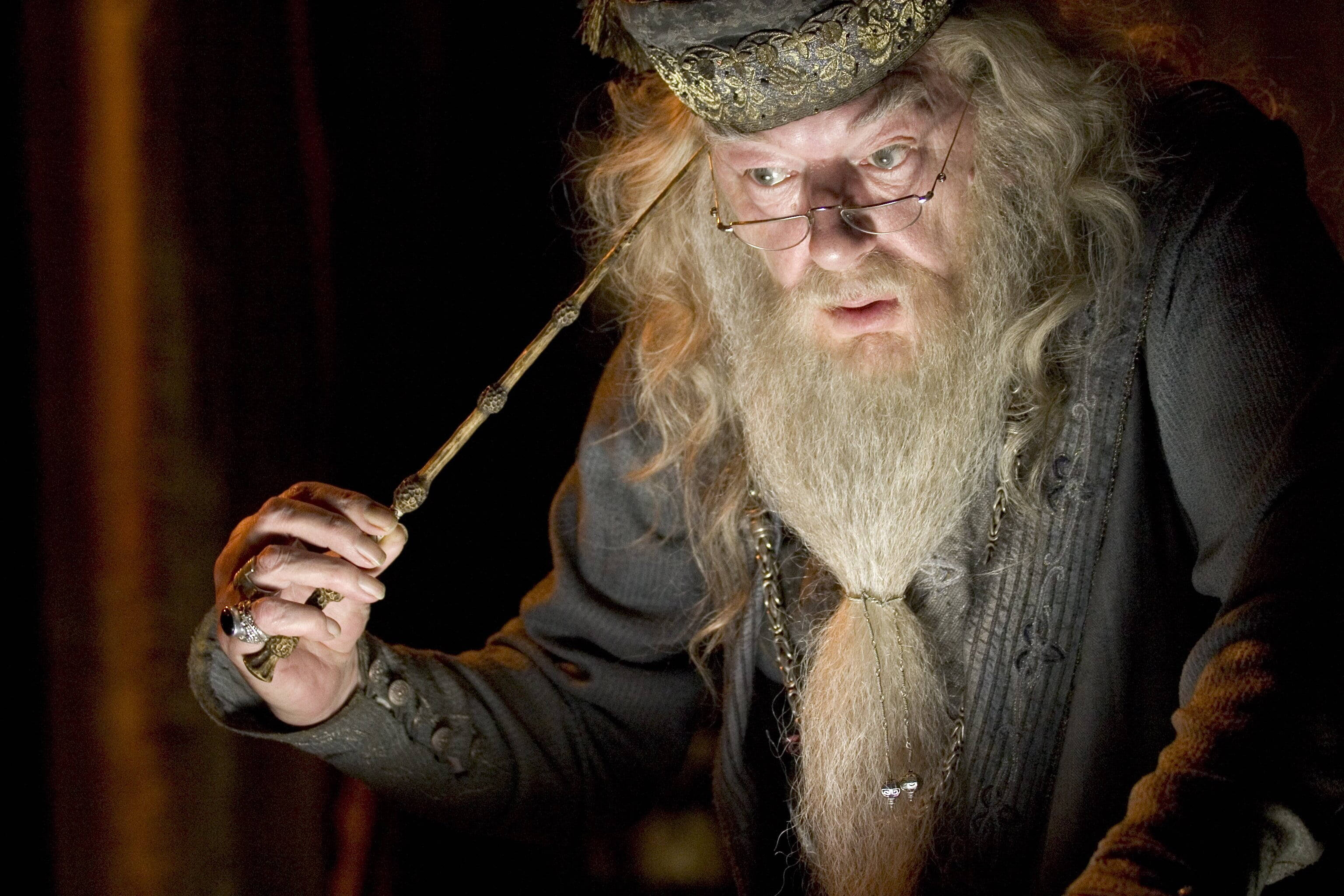 dumbledore 桌布 壁紙 — 一位長著長長白鬍鬚、戴著華麗帽子的巫師，在昏暗的房間裡拿著魔杖。
