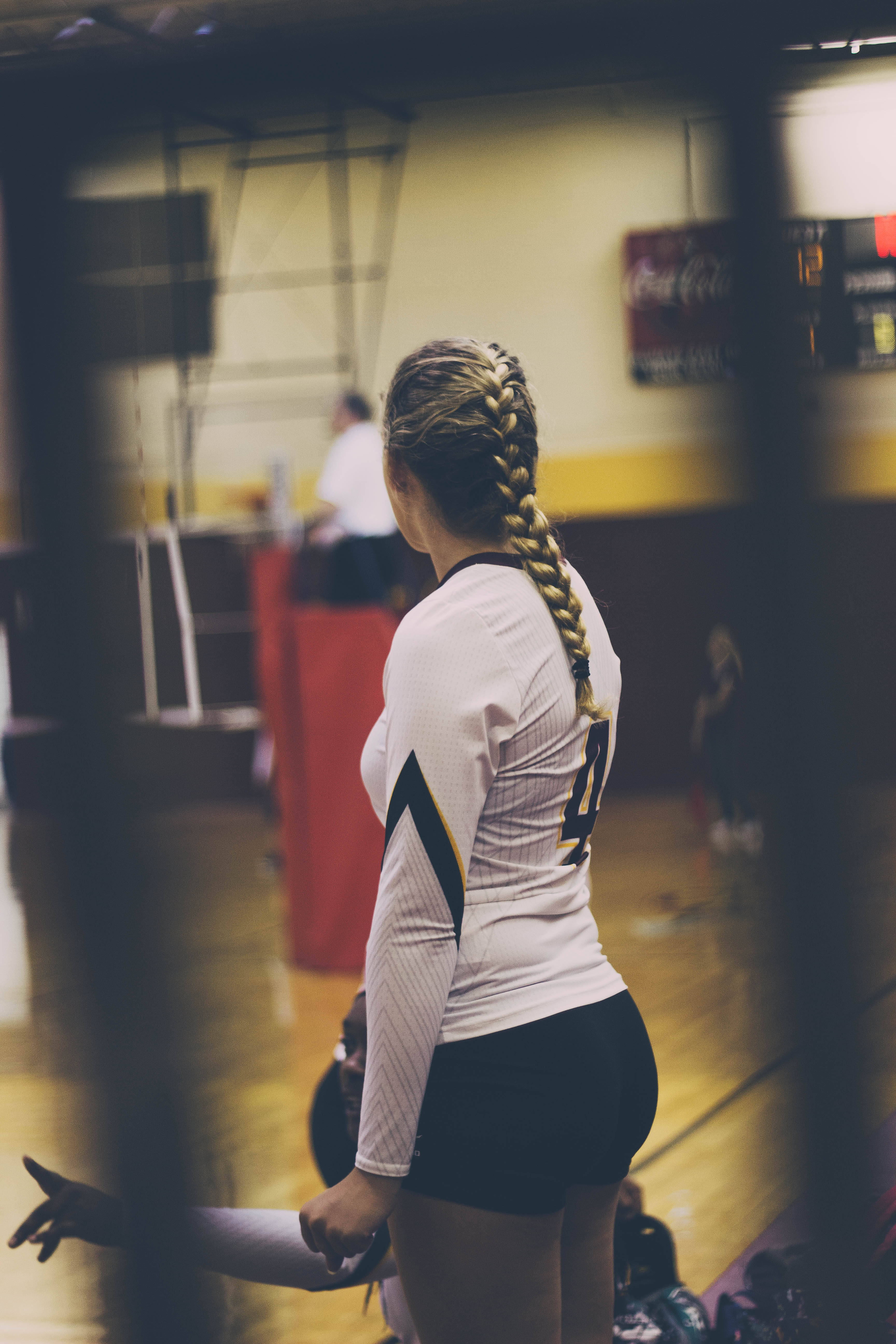 volleyball 4K 桌布 壁紙 — 一位長辮子馬尾的女排球運動員站在體育館，身穿白色球衣，號碼是四號。