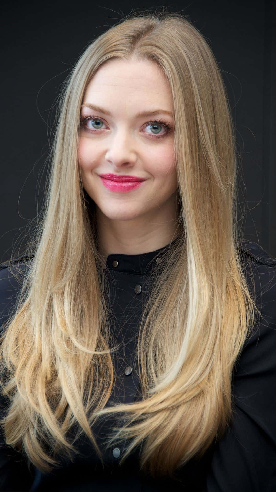 Amanda Seyfried 桌布 壁紙 — 一位長金髮、明亮藍眼睛的女性在深色背景下溫柔微笑的特寫肖像。