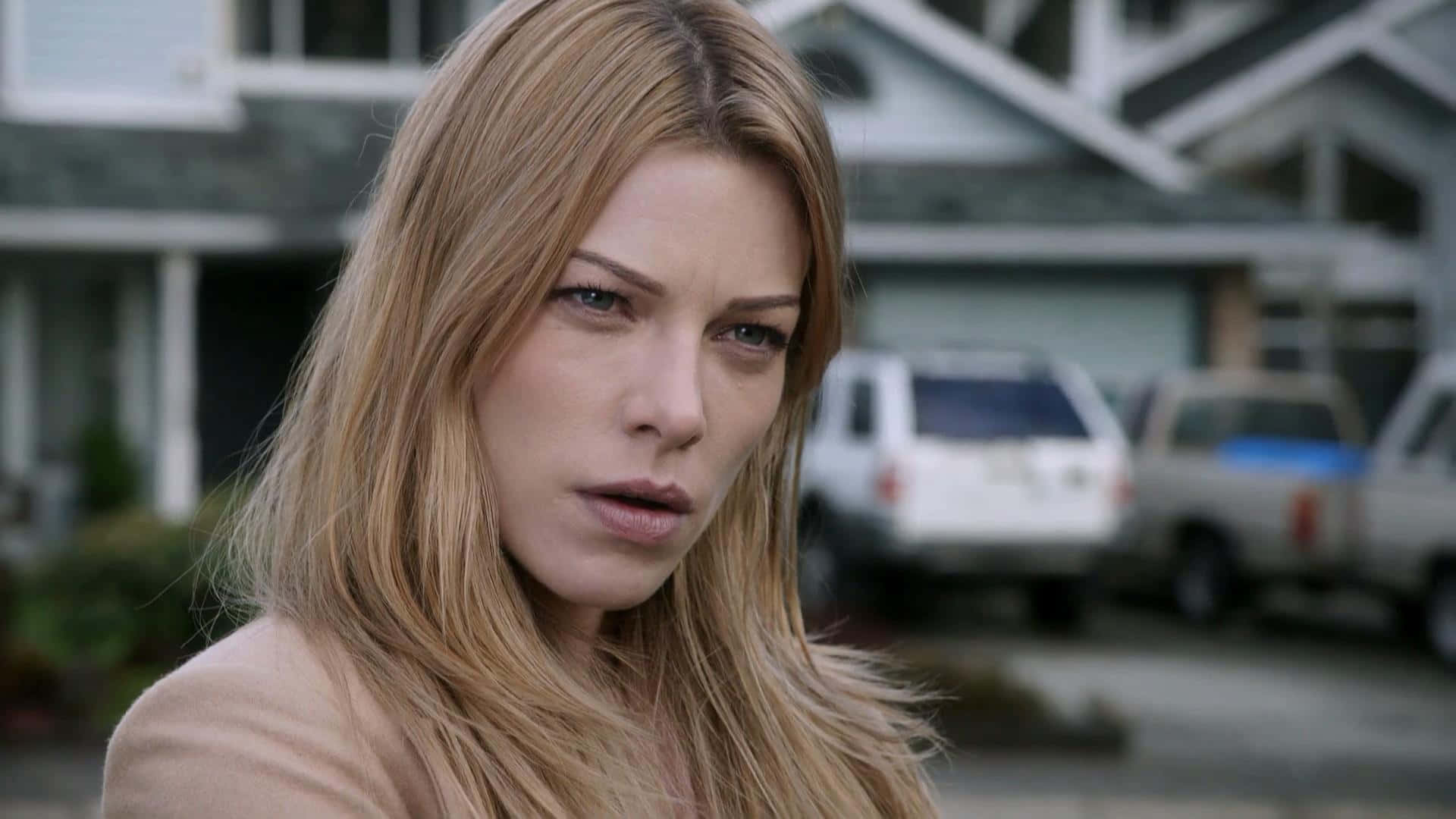 Lauren German 桌布 壁紙 — 一位長金髮女性在郊區車道上，身後有停泊的車輛，專注地向前凝視。