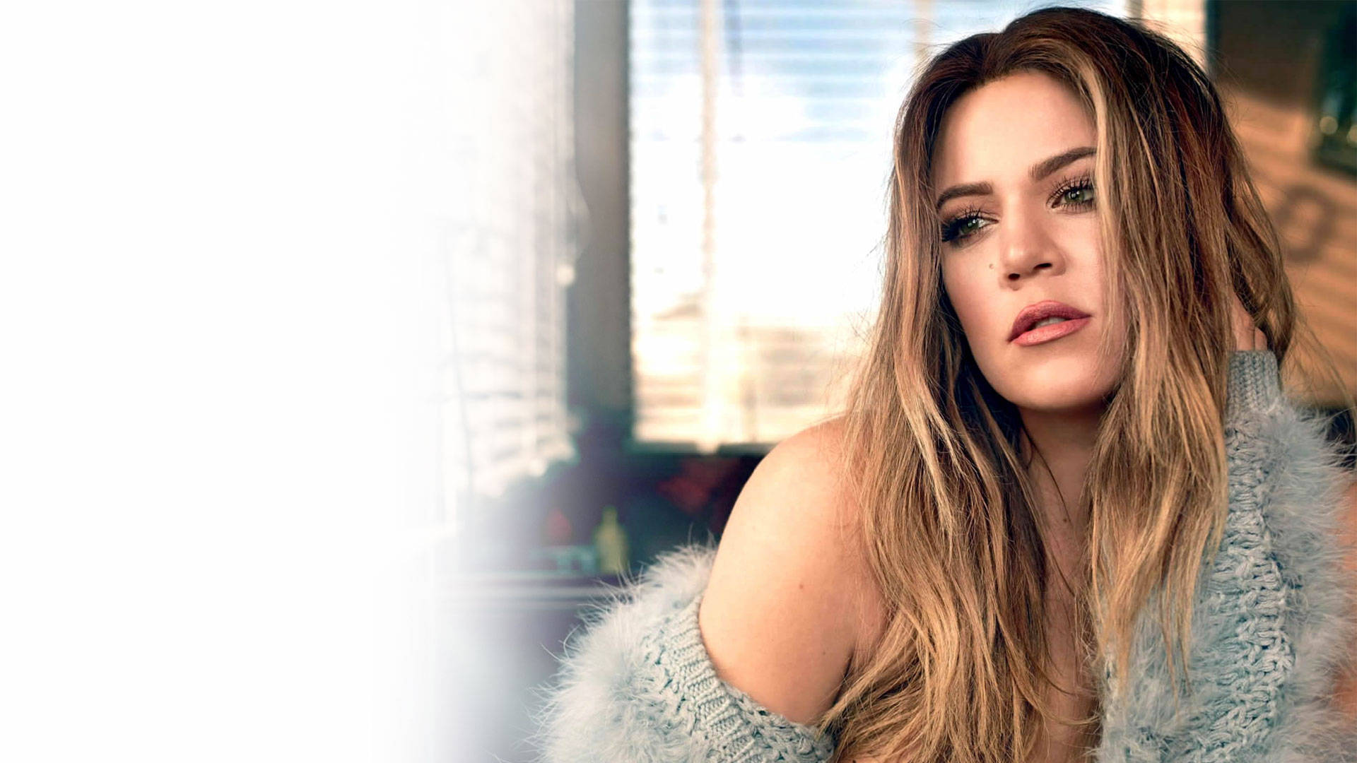 khloe 桌布 壁紙 — 一位長金髮的女性在窗邊穿著毛絨絨的淺藍色毛衣，若有所思地凝視著。