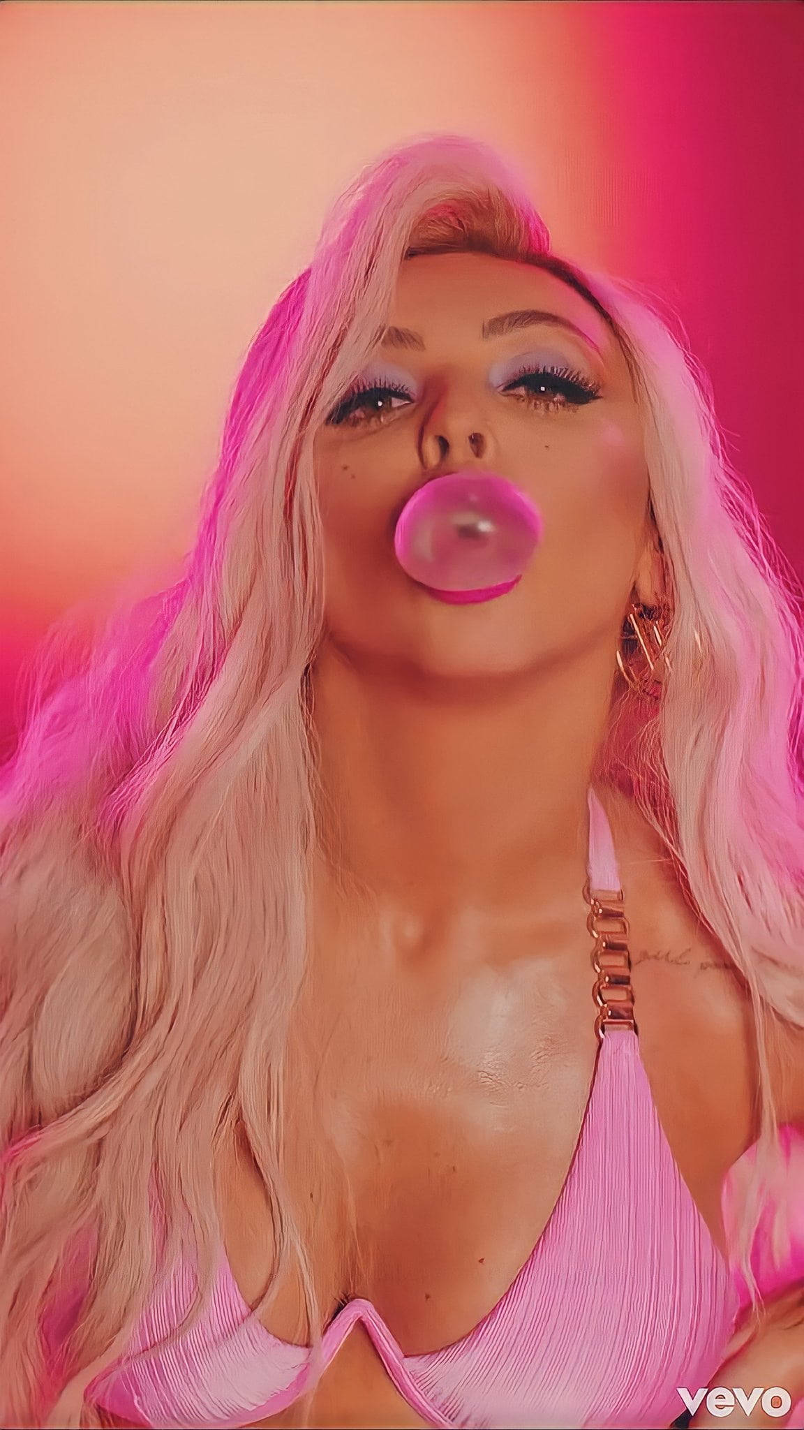 Jesy Nelson 桌布 壁紙 — 一位長金髮的女性在粉紅和橙色漸變背景前吹出粉紅色泡泡糖泡泡。