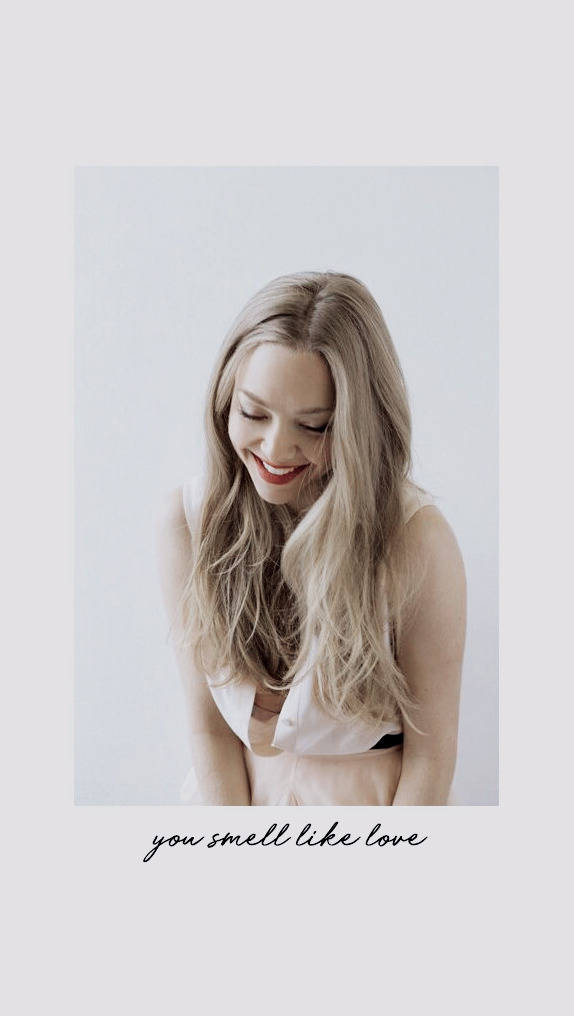 Amanda Seyfried 桌布 壁紙 — 一位長金髮的女性在純白背景前溫暖微笑，下方有文字。