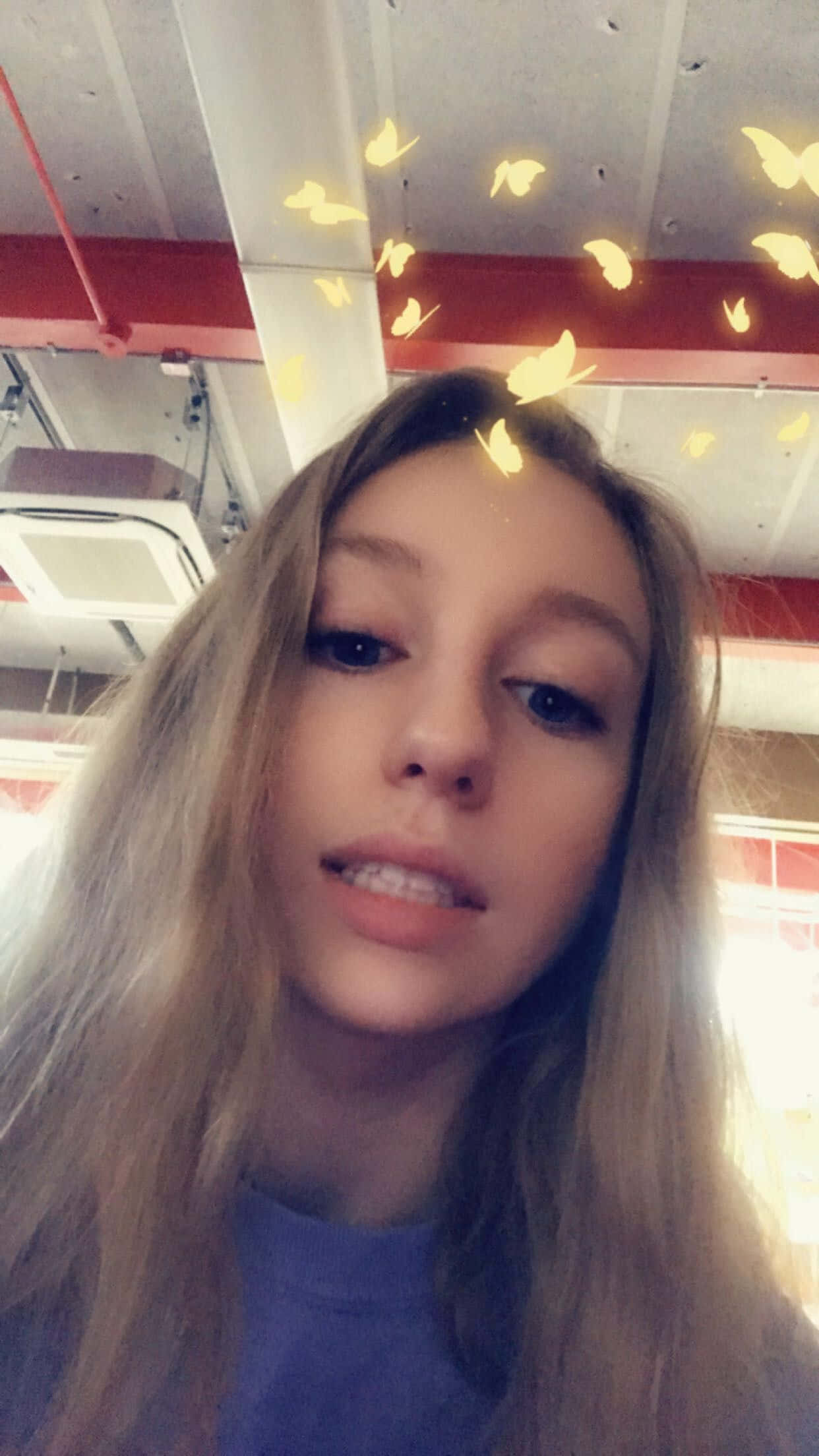 Snapchat 桌布 壁紙 — 一位長金髮的年輕女子看著鏡頭，發光的黃色蝴蝶在室內圍繞她的頭部飄浮。