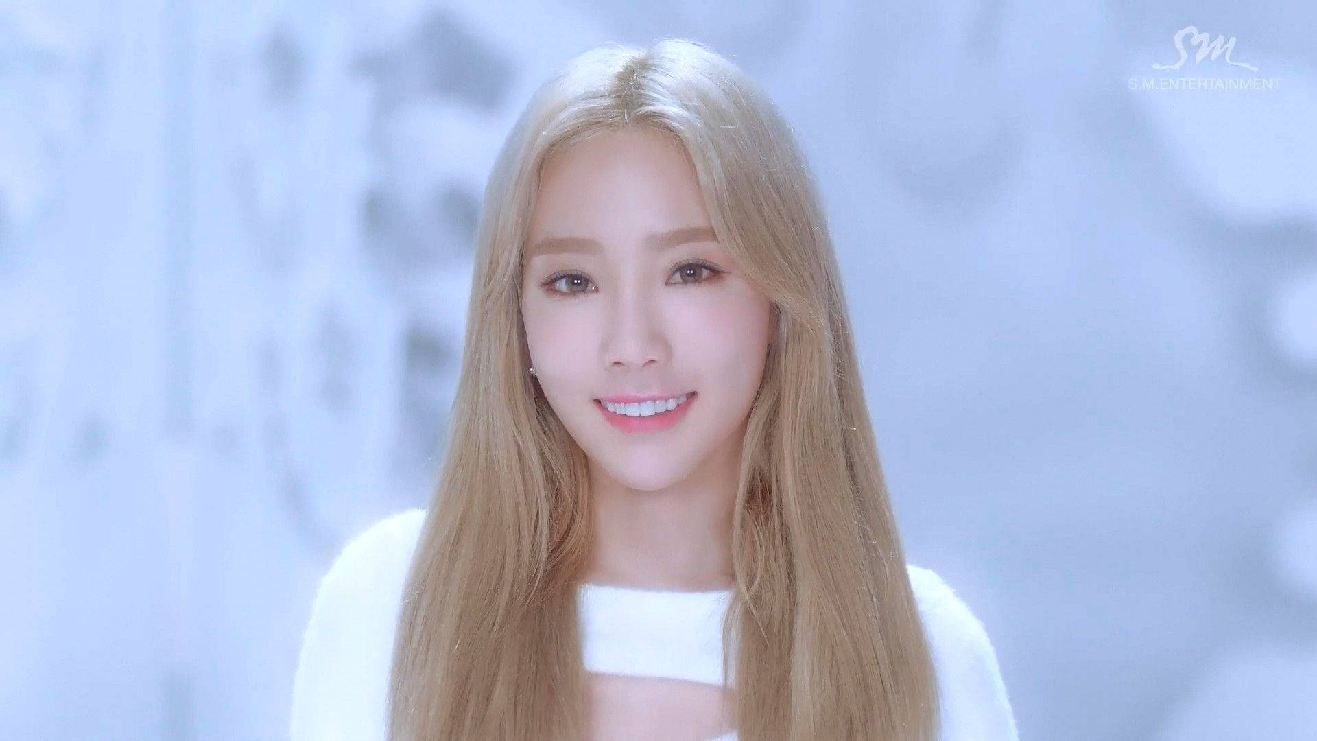 Taeyeon 桌布 壁紙 — 一位長金髮的年輕女性在柔和模糊的冰藍色背景下溫暖地微笑。