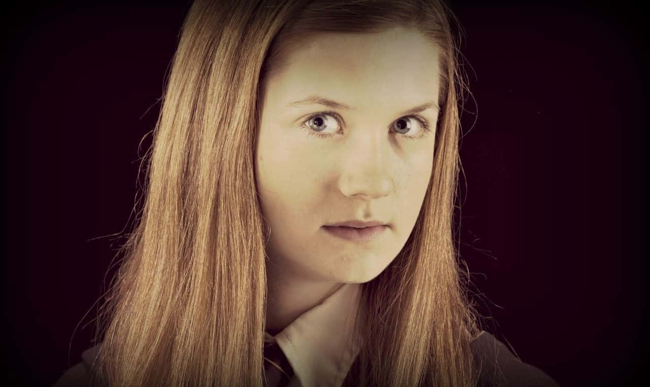 Ginny Weasley 桌布 壁紙 — 一位長金髮的年輕女性在柔和燈光下，對著深酒紅色背景專注地凝視。