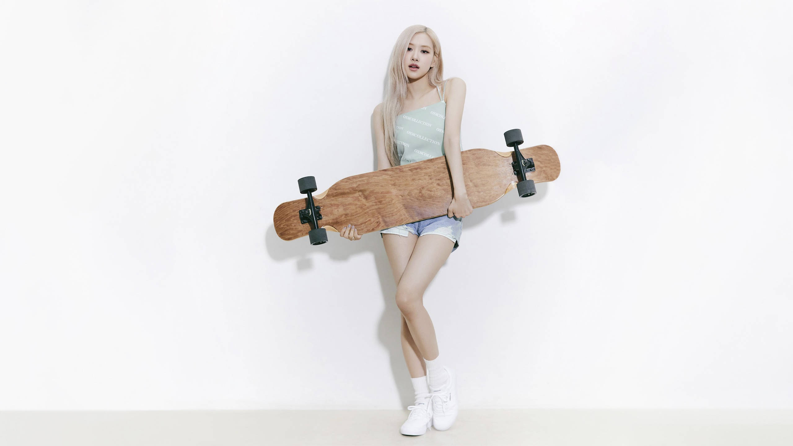 blackpink rose 桌布 壁紙 — 一位長金髮的年輕女性在簡約的工作室環境中，將木製長板靠在純白牆上。