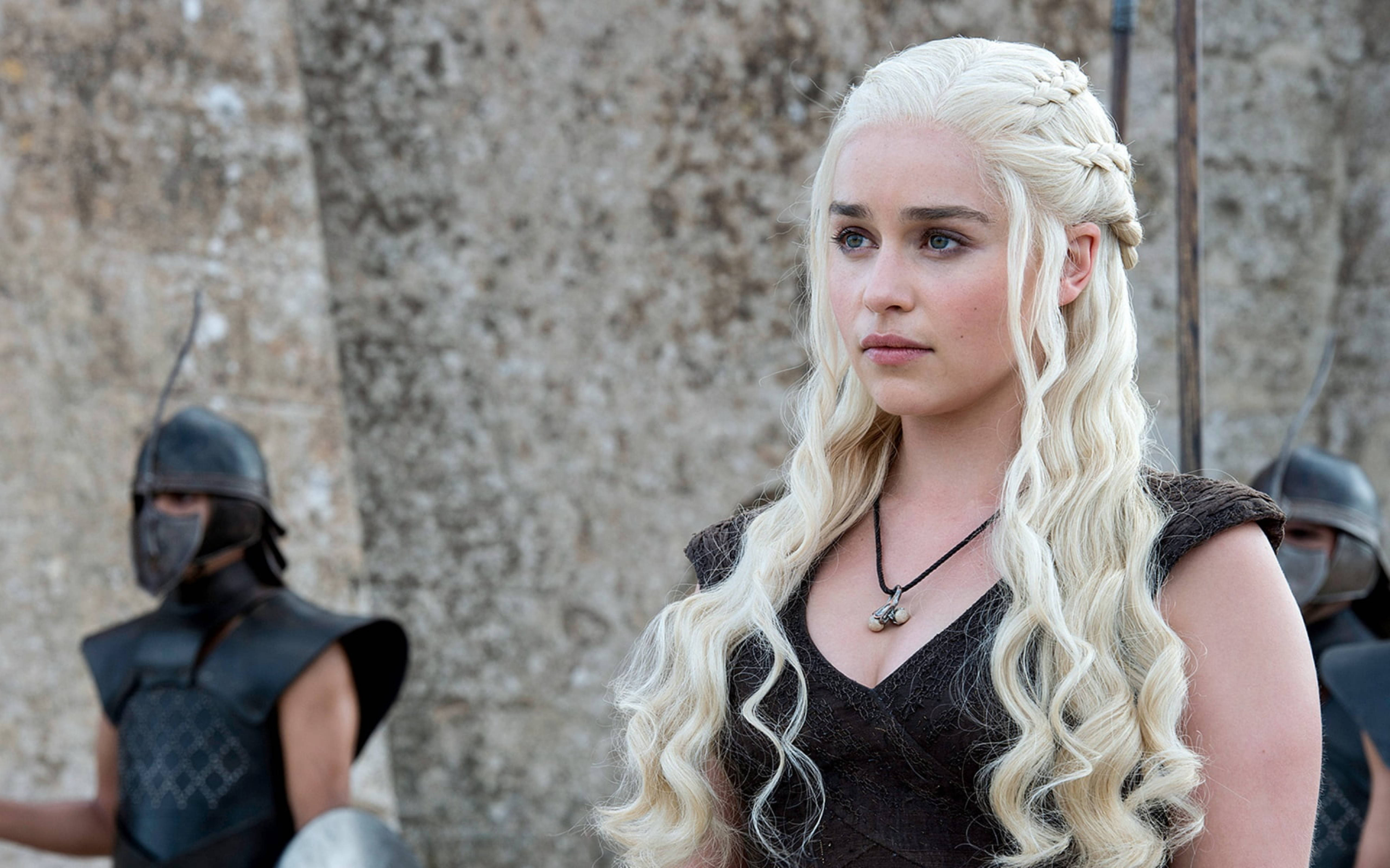 daenerys 桌布 壁紙 — 一位長金髮辮的女性站在石牆前，背景有裝甲守衛。