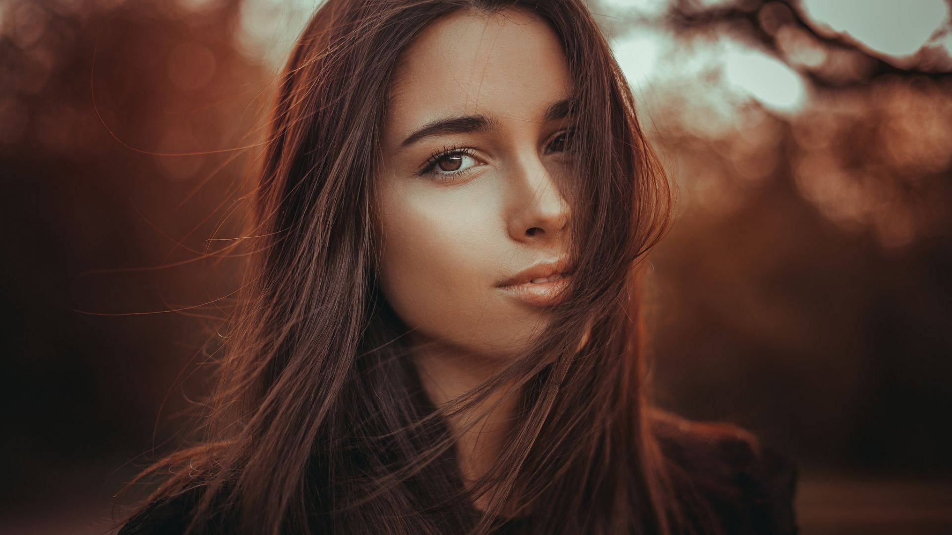 Brown 桌布 壁紙 — 一位長長棕色頭髮的女性，在溫暖模糊的秋季背景下，溫柔地凝視著相機。