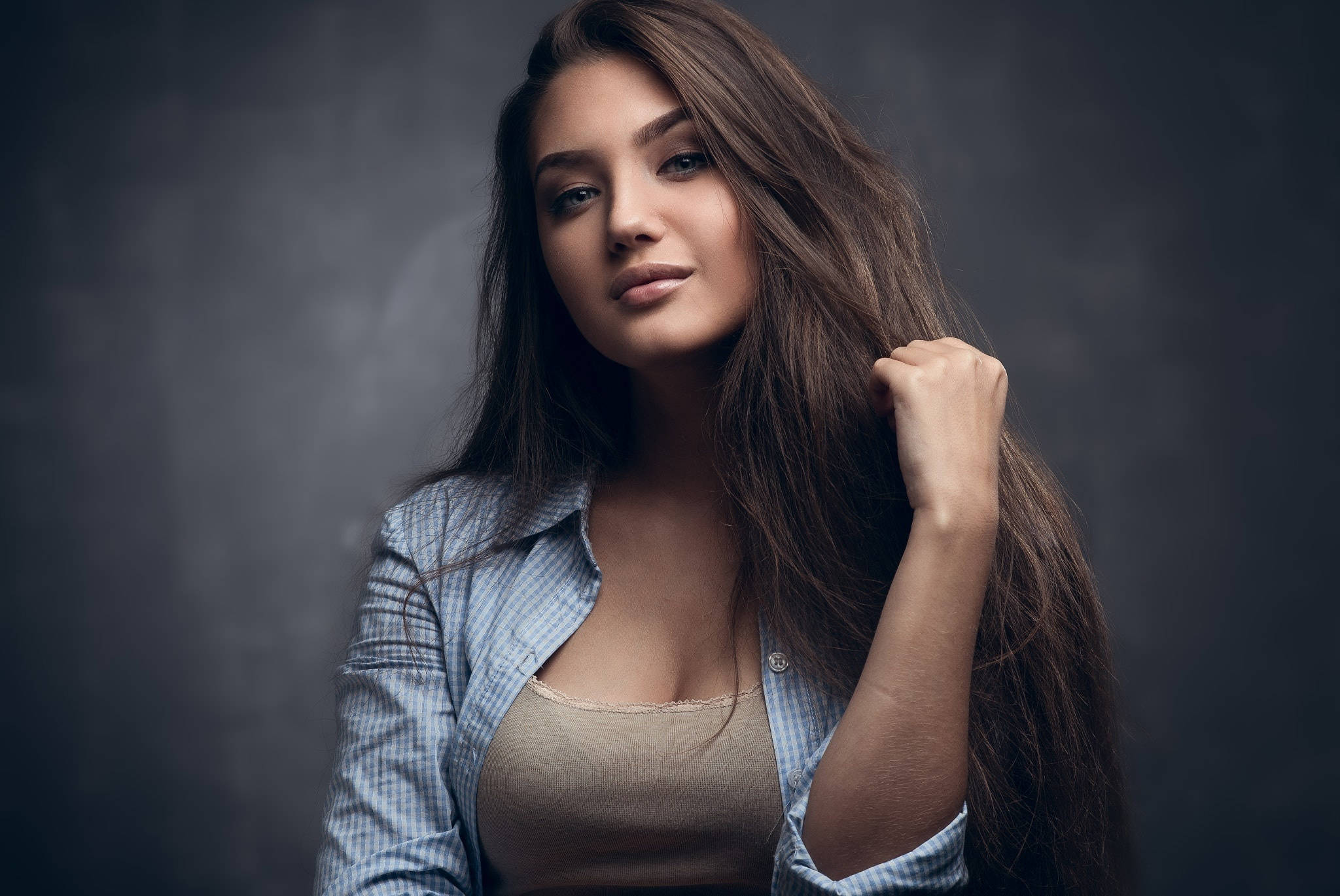 Woman 桌布 壁紙 — 一位長長棕色頭髮的女性在深灰色工作室背景前輕輕觸摸頭髮，同時看著相機。