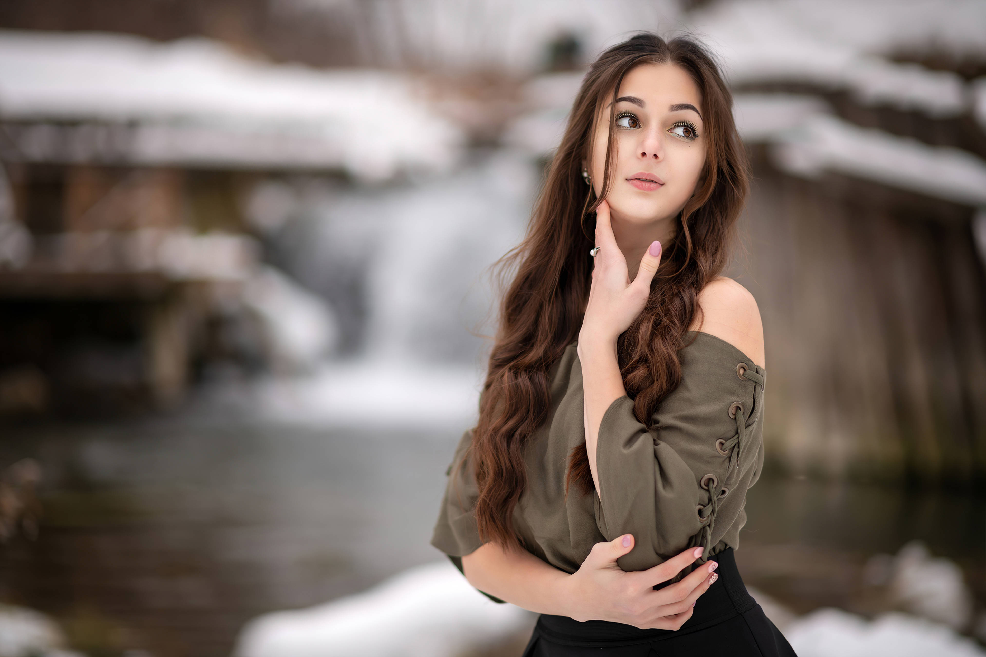 美女 桌布 壁紙 — 一位長長棕色頭髮的年輕女子站在雪瀑布旁，帶著沉思的表情向上凝望。