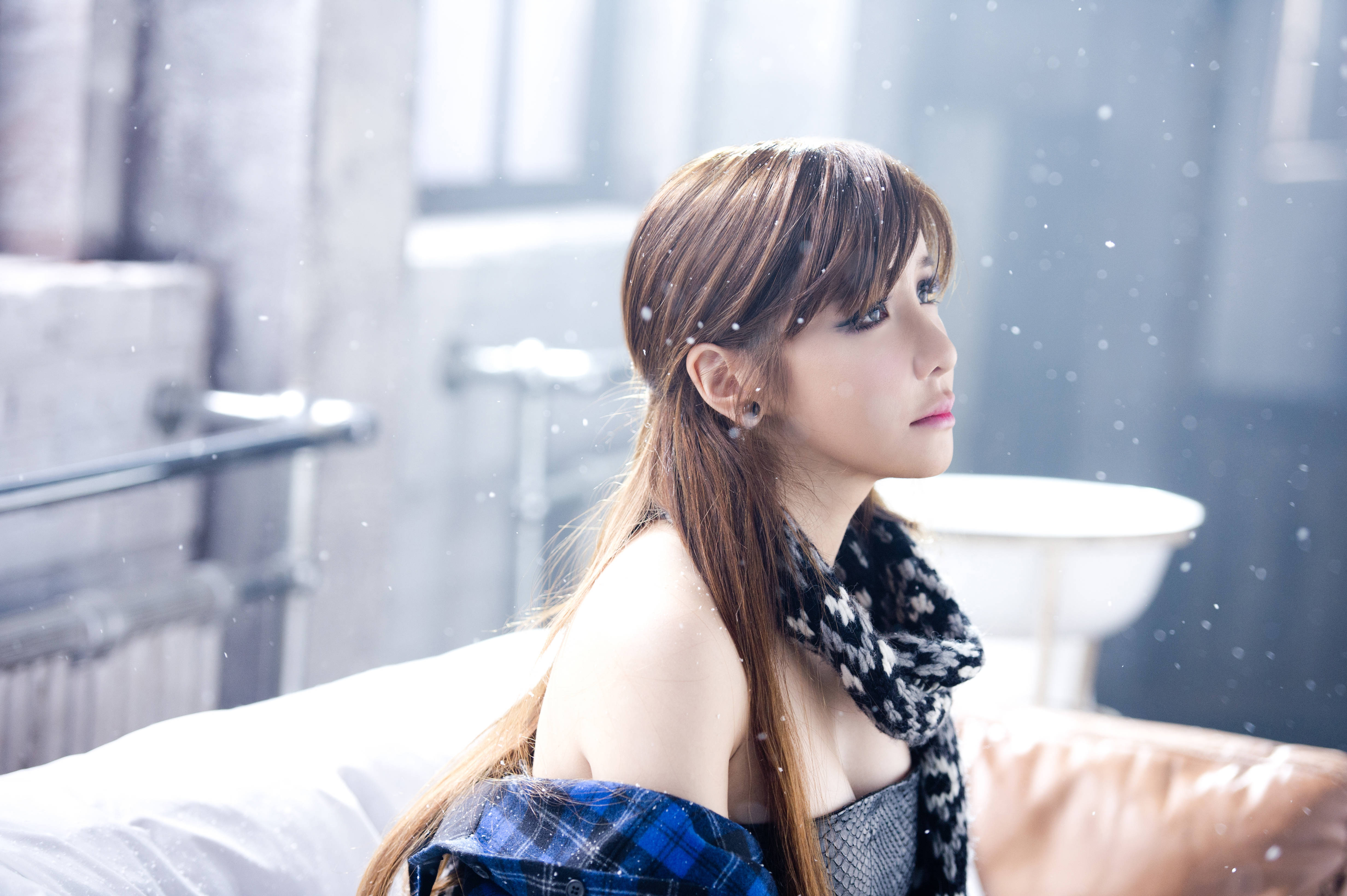 2ne1 桌布 壁紙 — 一位長長棕色頭髮的年輕女性坐在雪景房間的床上，戴著圍巾和格子襯衫，若有所思地凝視窗外。