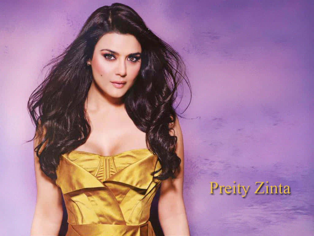 Preity Zinta 桌布 壁紙 — 一位長長深色波浪髮的女性，穿著金色無肩帶連衣裙，背景是柔和的紫色紋理。