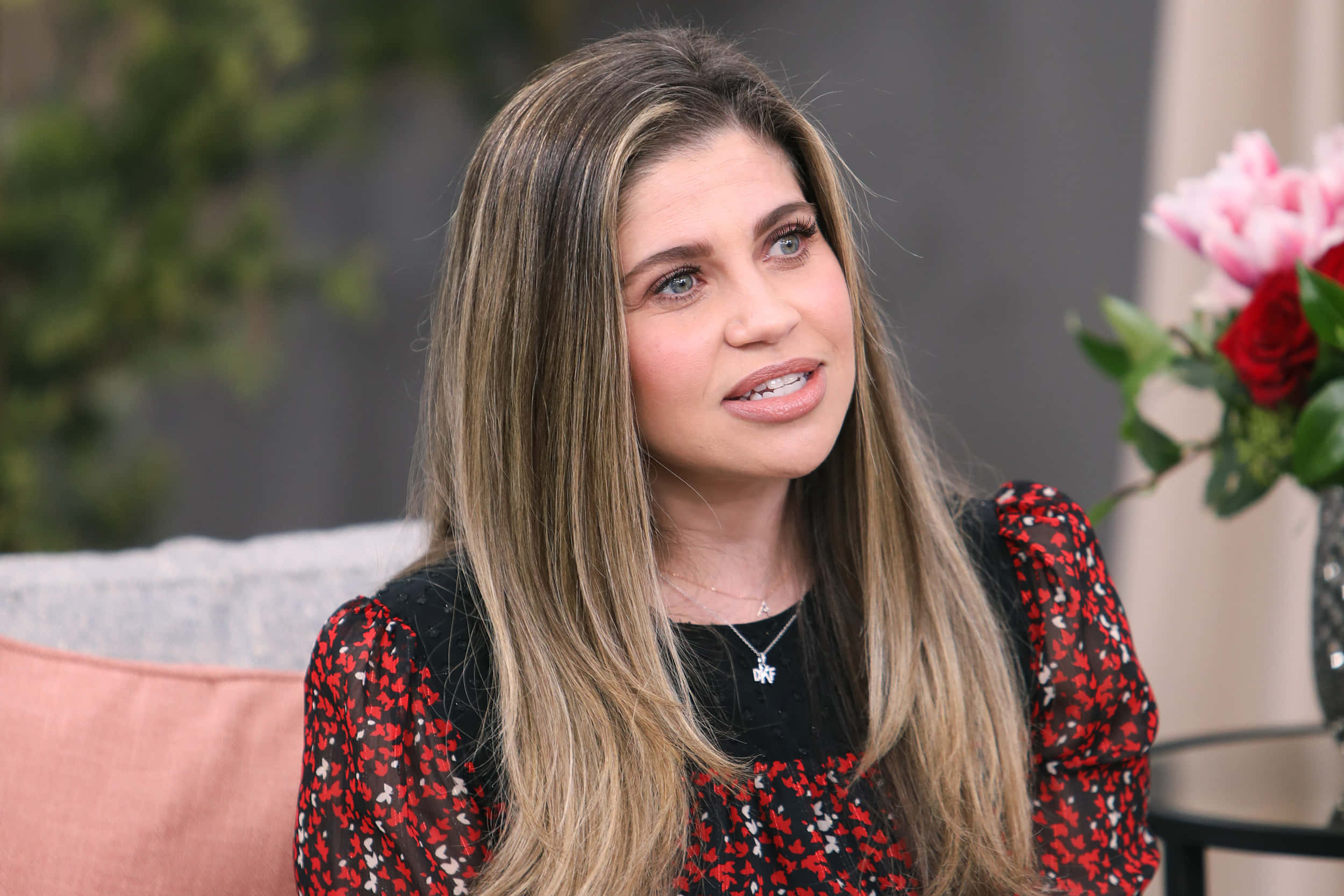 Danielle Fishel 桌布 壁紙 — 一位長長金髮、身穿紅色花卉上衣的女性坐在沙發上，旁邊放著一瓶粉紅和紅色的玫瑰。