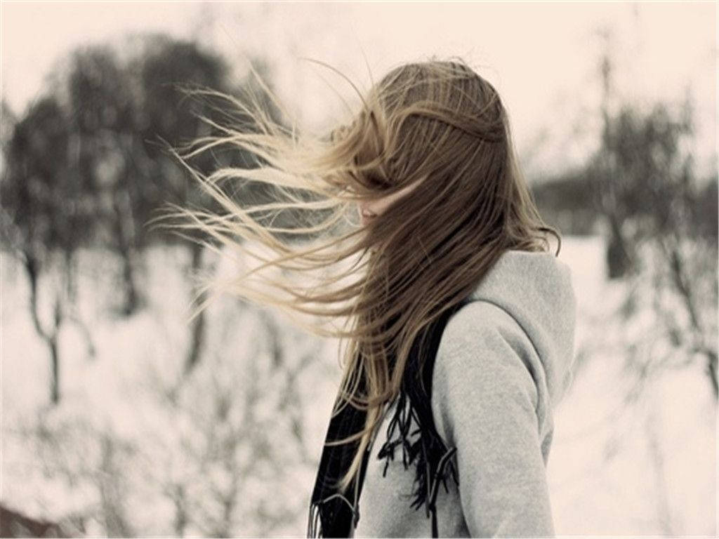 Sad Girl 桌布 壁紙 — 一位長長金髮被風吹拂的女性，站在白雪覆蓋的冬季景觀中，周圍是光禿禿的樹木。