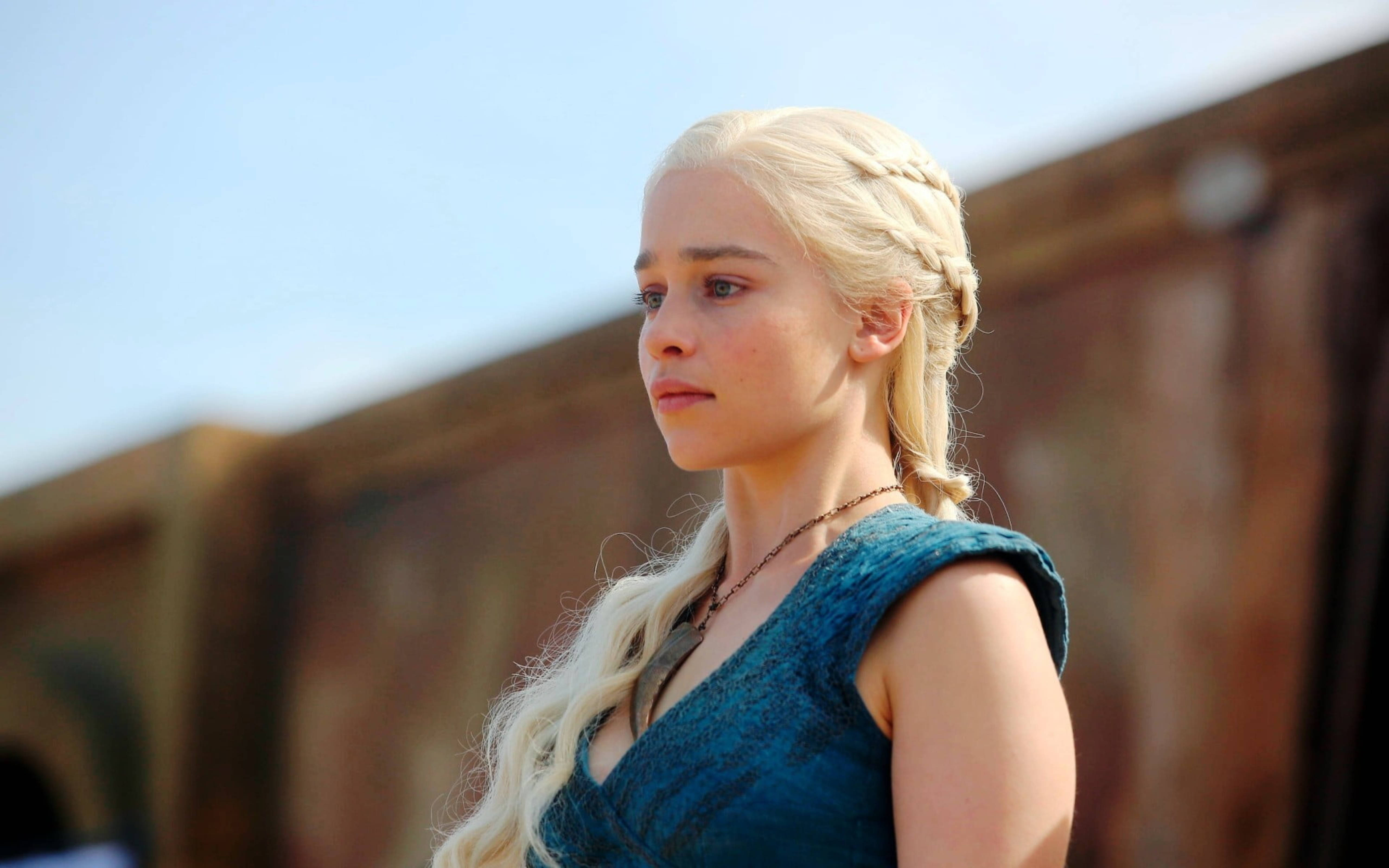 daenerys 桌布 壁紙 — 一位長長金髮辮子的女人穿著青綠色連衣裙，在晴朗的藍天下，靠著木結構望向遠方。