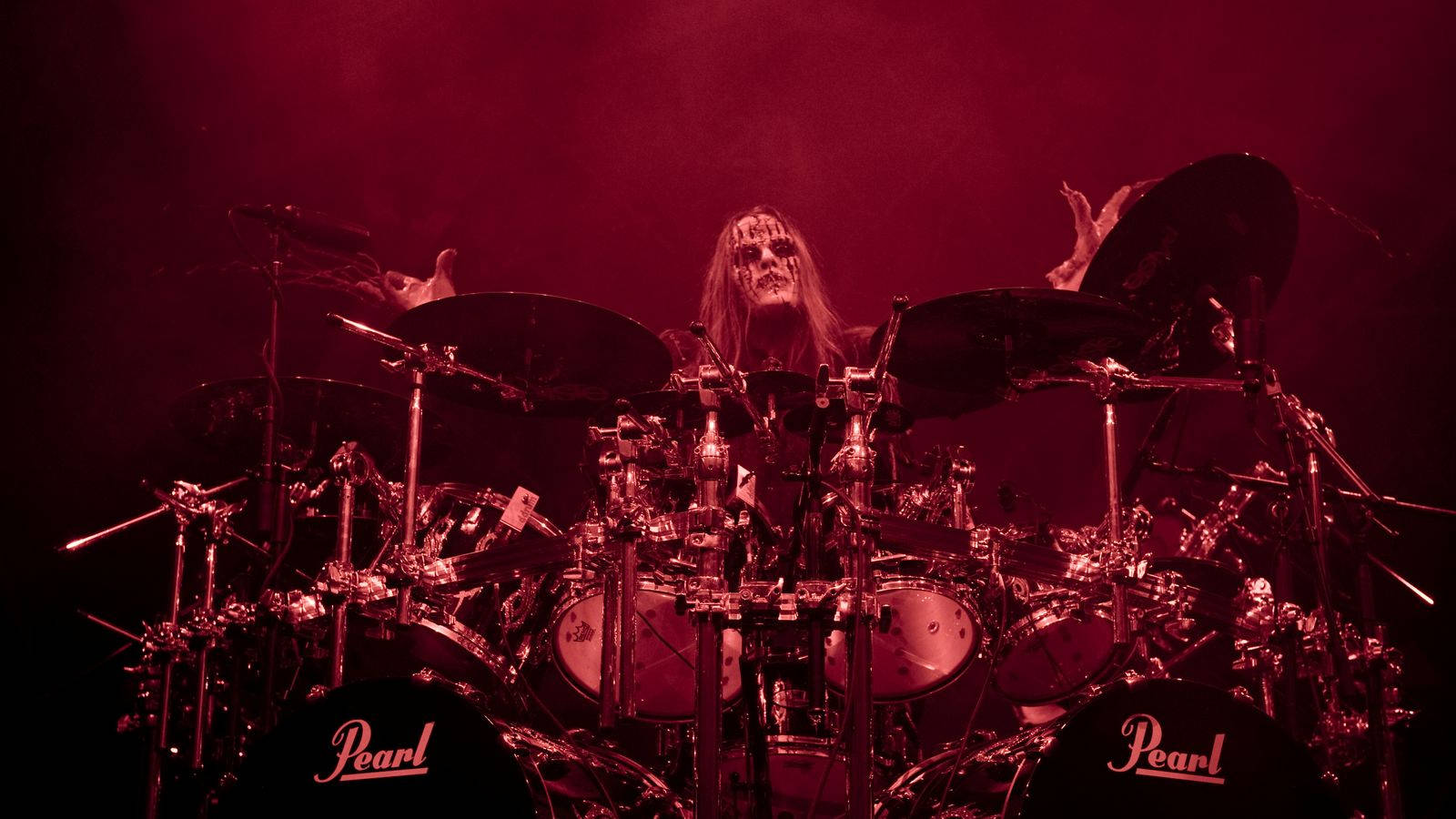 Slipknot 桌布 壁紙 — 一位長髮、骷髏妝容的鼓手在強烈的紅色舞台燈光下演奏Pearl鼓組。