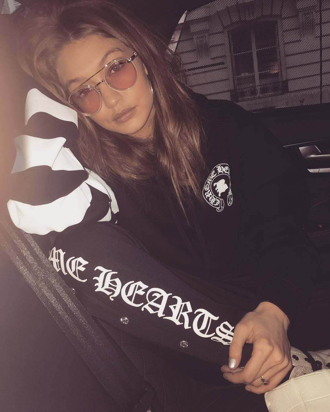 Chrome Hearts 桌布 壁紙 — 一位長髮女子戴著粉紅色太陽眼鏡，身穿帶有白色字樣和骷髏圖案的黑色外套，在車內休息。
