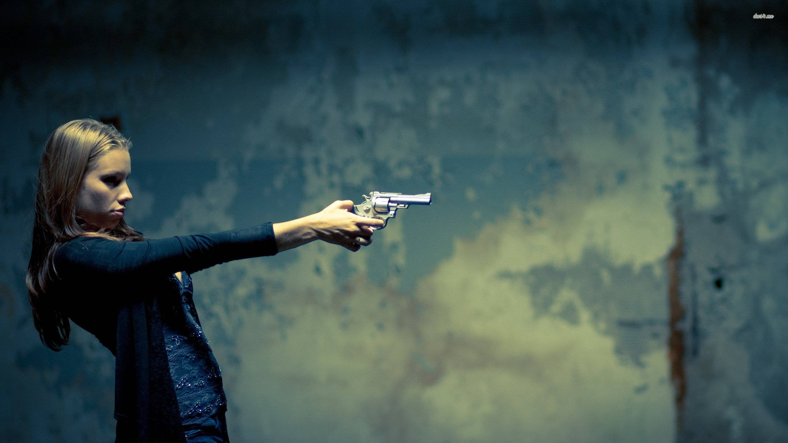 Shooting 桌布 壁紙 — 一位長髮女性在昏暗燈光下，用銀色左輪手槍瞄準一面風化的藍黃色牆壁。