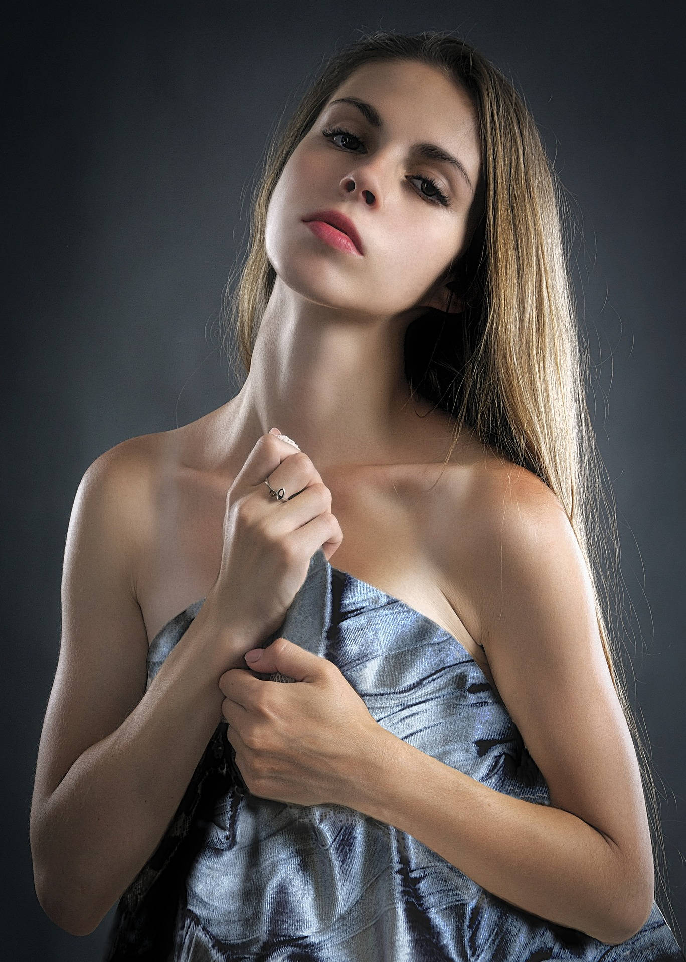 Photoshoot 桌布 壁紙 — 一位長髮女性在深色背景下抬頭仰望，同時調整肩上閃爍的銀色布料。