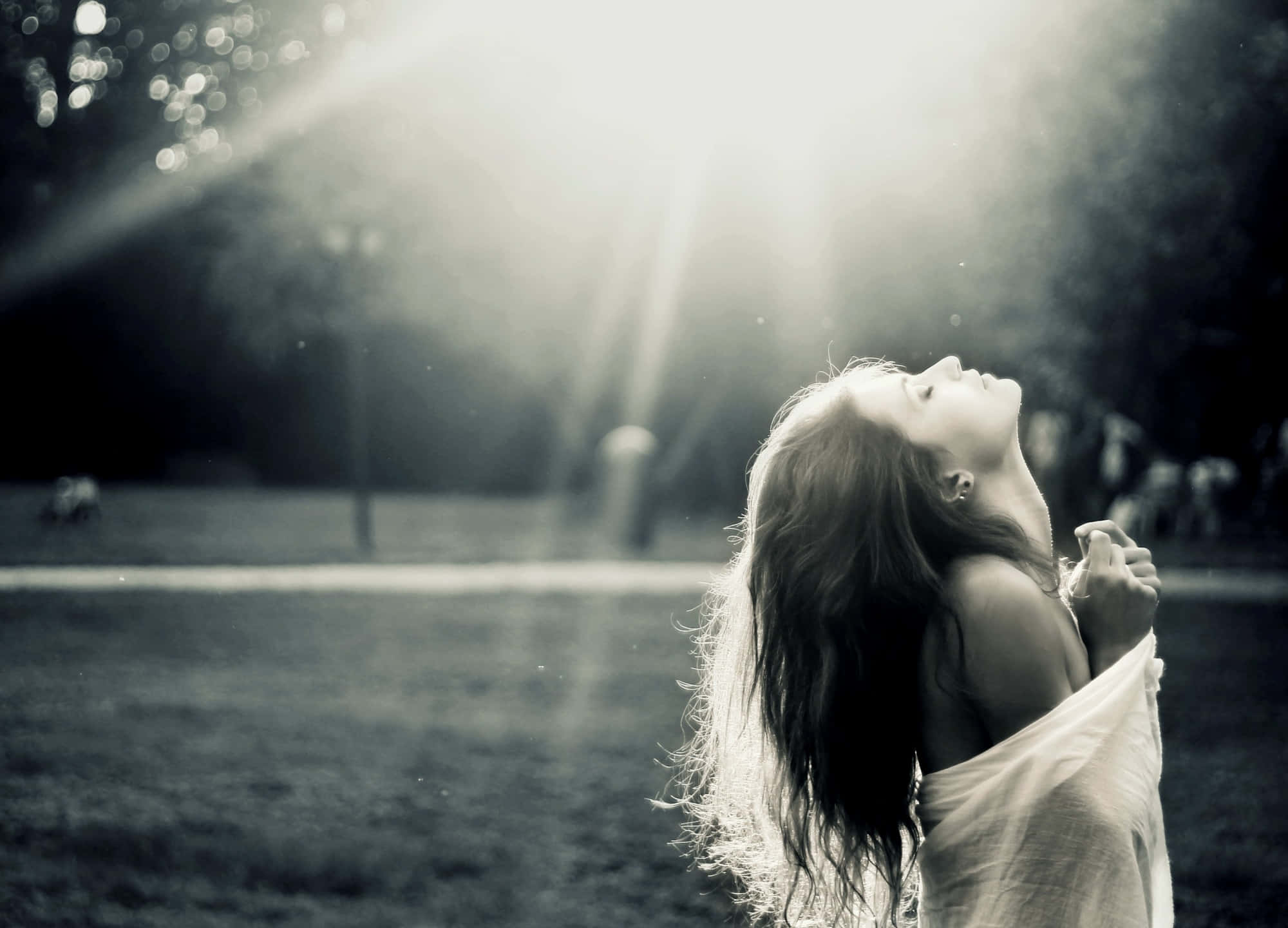 Alone 桌布 壁紙 — 一位長髮女性站在陽光普照的公園裡，頭向後仰，金色光線照亮她的臉龐和秀髮。