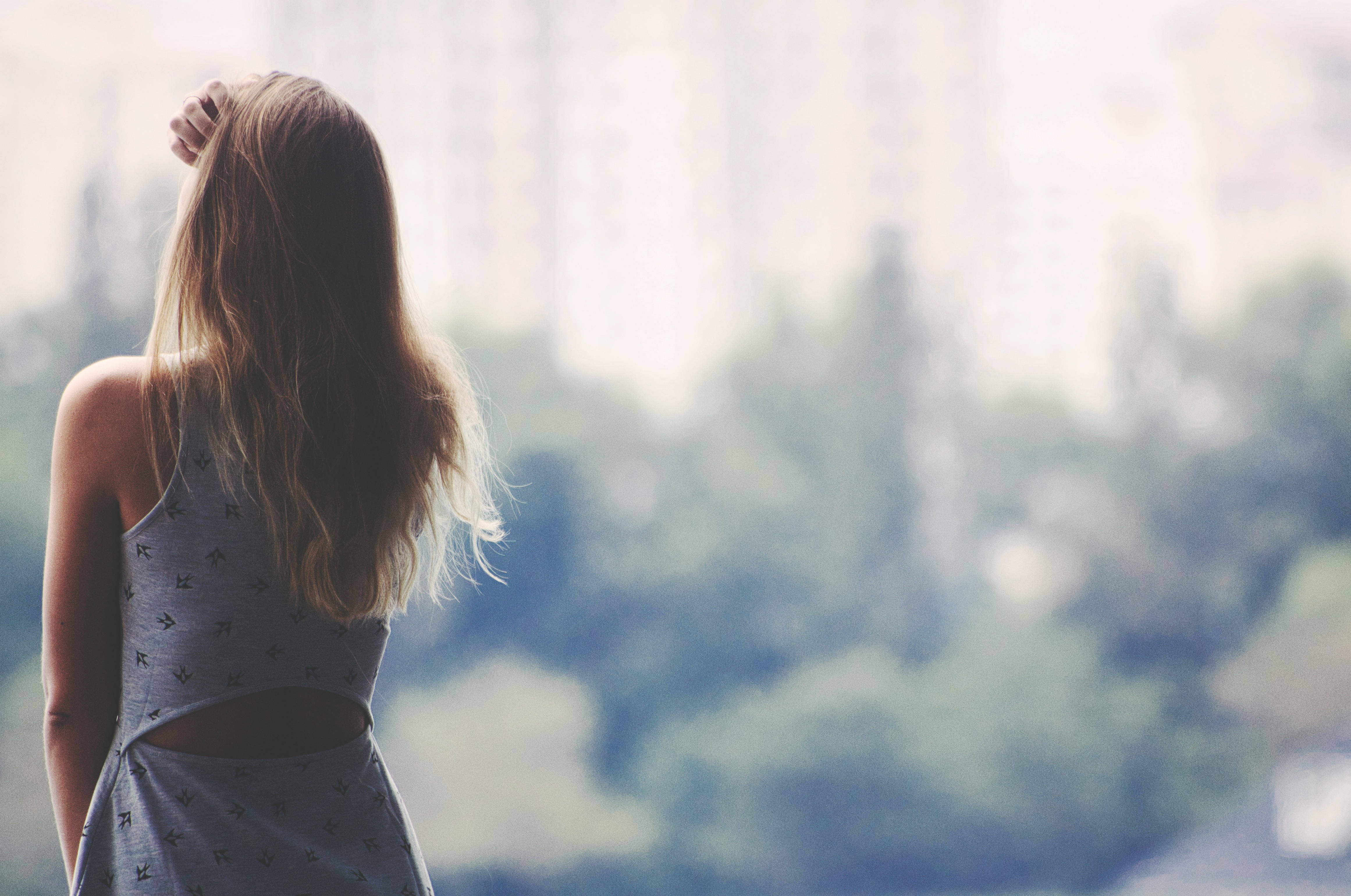 girls 桌布 壁紙 — 一位長髮女性背對鏡頭，凝視著沐浴在柔和日光中的模糊城市景觀。