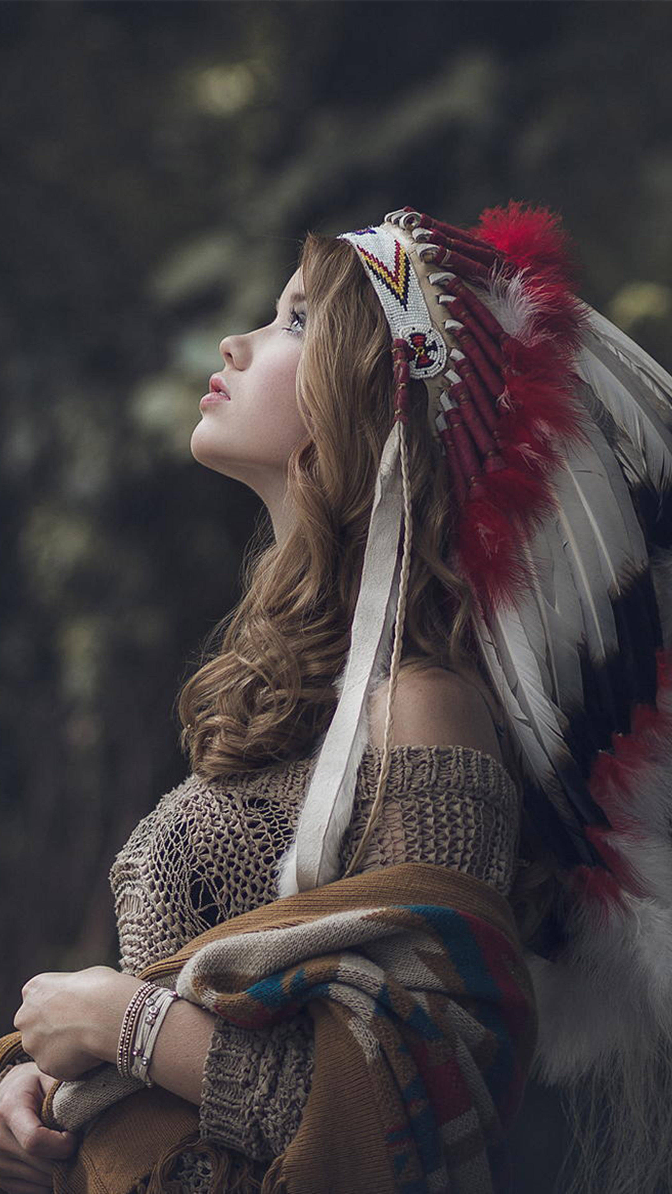 Native American 桌布 壁紙 — 一位長髮年輕女性戴著紅白羽毛頭飾和針織上衣，在森林中向上凝望。
