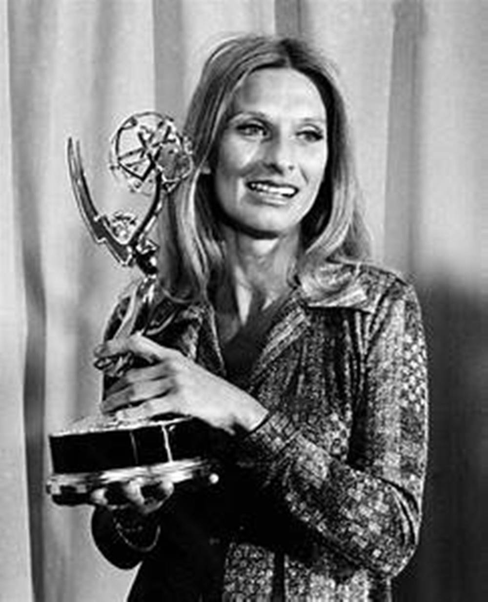 Cloris Leachman 桌布 壁紙 — 一位長髮微笑的女性，在垂簾背景下手持艾美獎的經典黑白肖像。