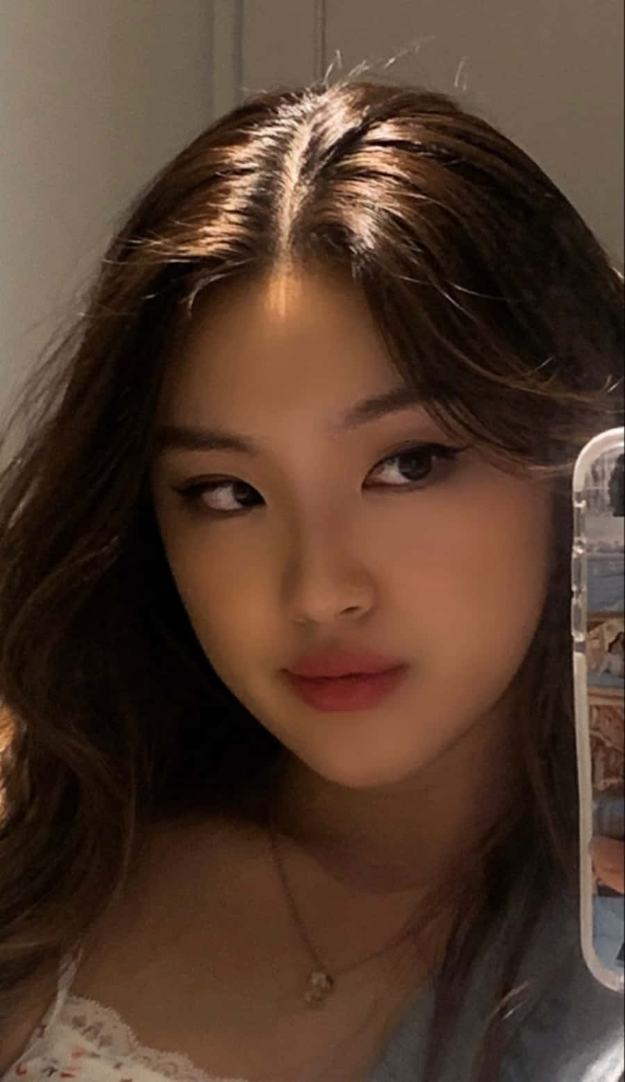 美女 桌布 壁紙 — 一位長髮棕眼、妝容柔和的年輕女性在溫暖燈光的自拍中直視鏡頭。