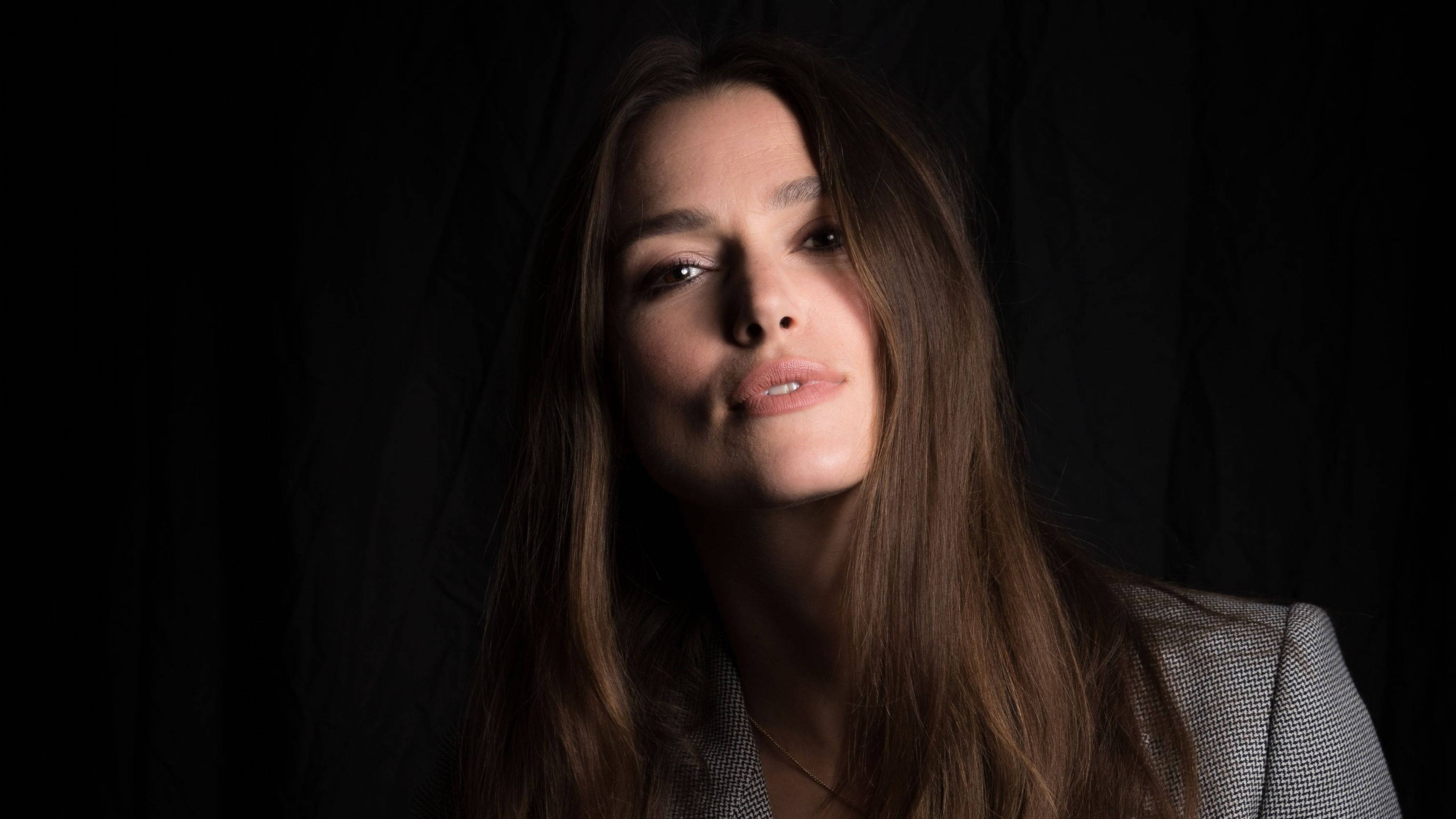 Keira Knightley 桌布 壁紙 — 一位長髮棕眼的女性在純黑背景下溫柔凝視，她的臉被戲劇性的工作室燈光照亮。