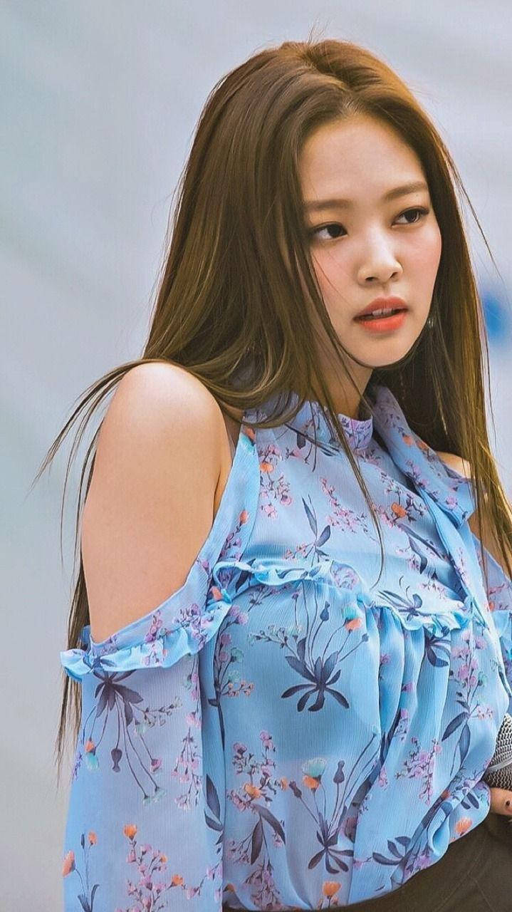 Jennie 桌布 壁紙 — 一位長髮棕眼的年輕女性，穿著淺藍色花卉荷葉邊露肩上衣，背景是柔和的灰色。