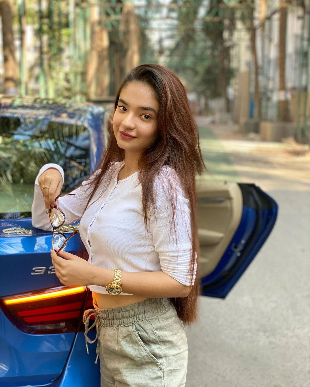 Indian 桌布 壁紙 — 一位長髮棕色的年輕女子站在一輛藍色汽車旁，手持太陽眼鏡，對著鏡頭微笑。