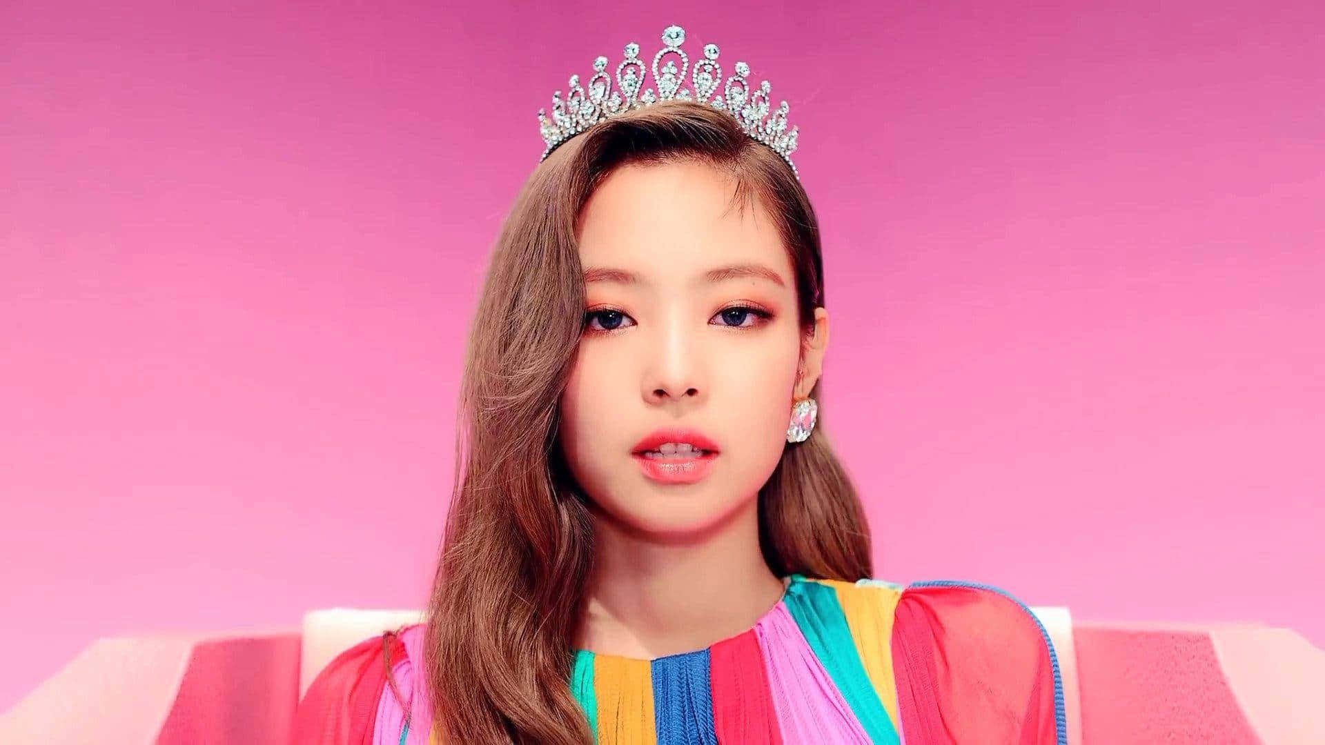 BLACKPINK 桌布 壁紙 — 一位長髮棕色的年輕女性，戴著閃亮的頭飾，穿著彩虹條紋連衣裙，背景為純粉色。
