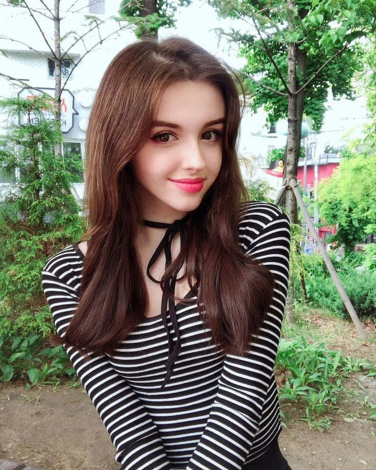 穿著條紋上衣的年輕女性在戶外樹旁微笑 — 漂亮的動圖 壁紙