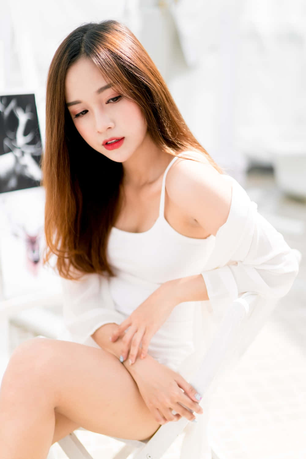 美女 桌布 壁紙 — 一位長髮棕色的年輕女性優雅地坐在白色椅子上，身穿白色露肩裝，身處明亮簡約的房間。