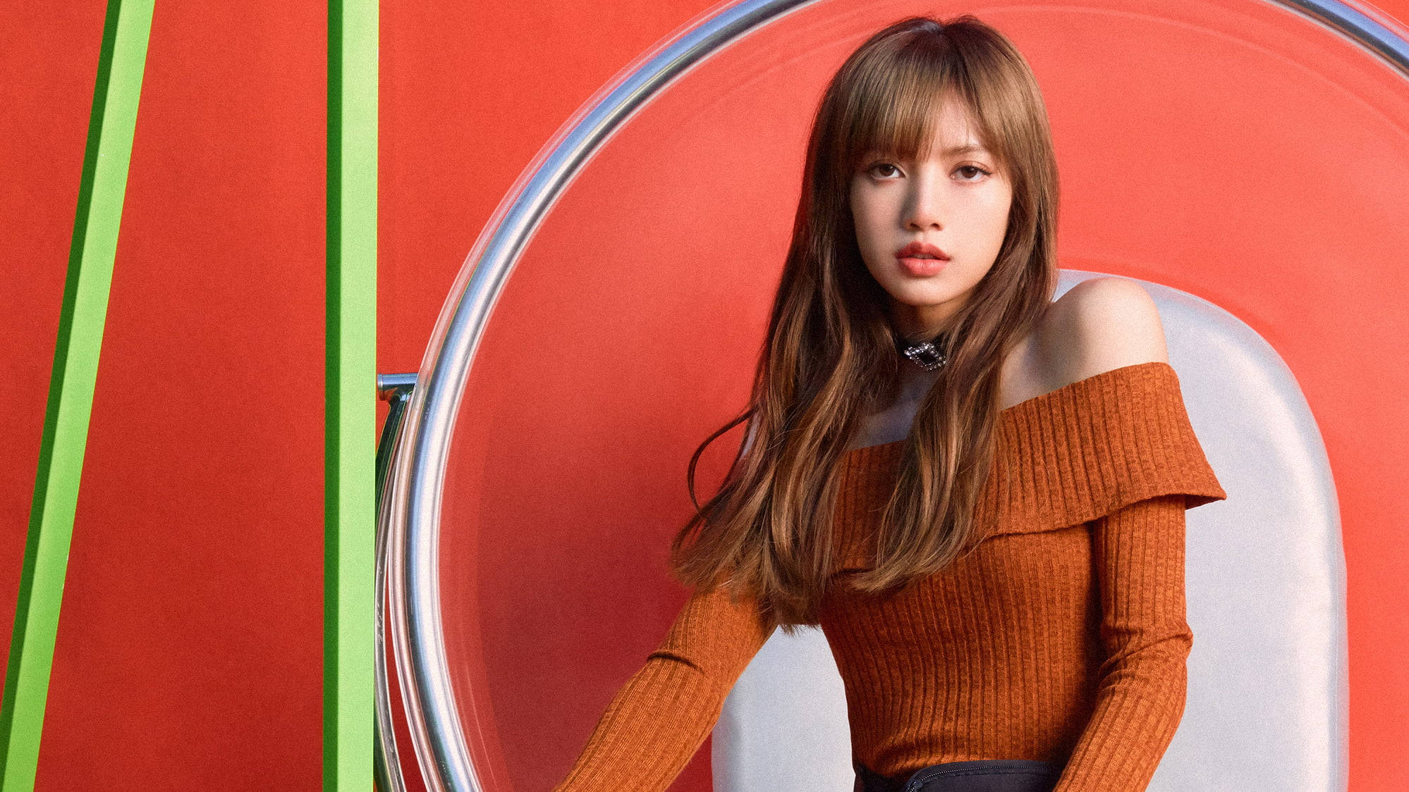 BLACKPINK 桌布 壁紙 — 一位長髮棕色的年輕女性坐在現代椅子上，背景是大膽的紅色和綠色幾何圖案。